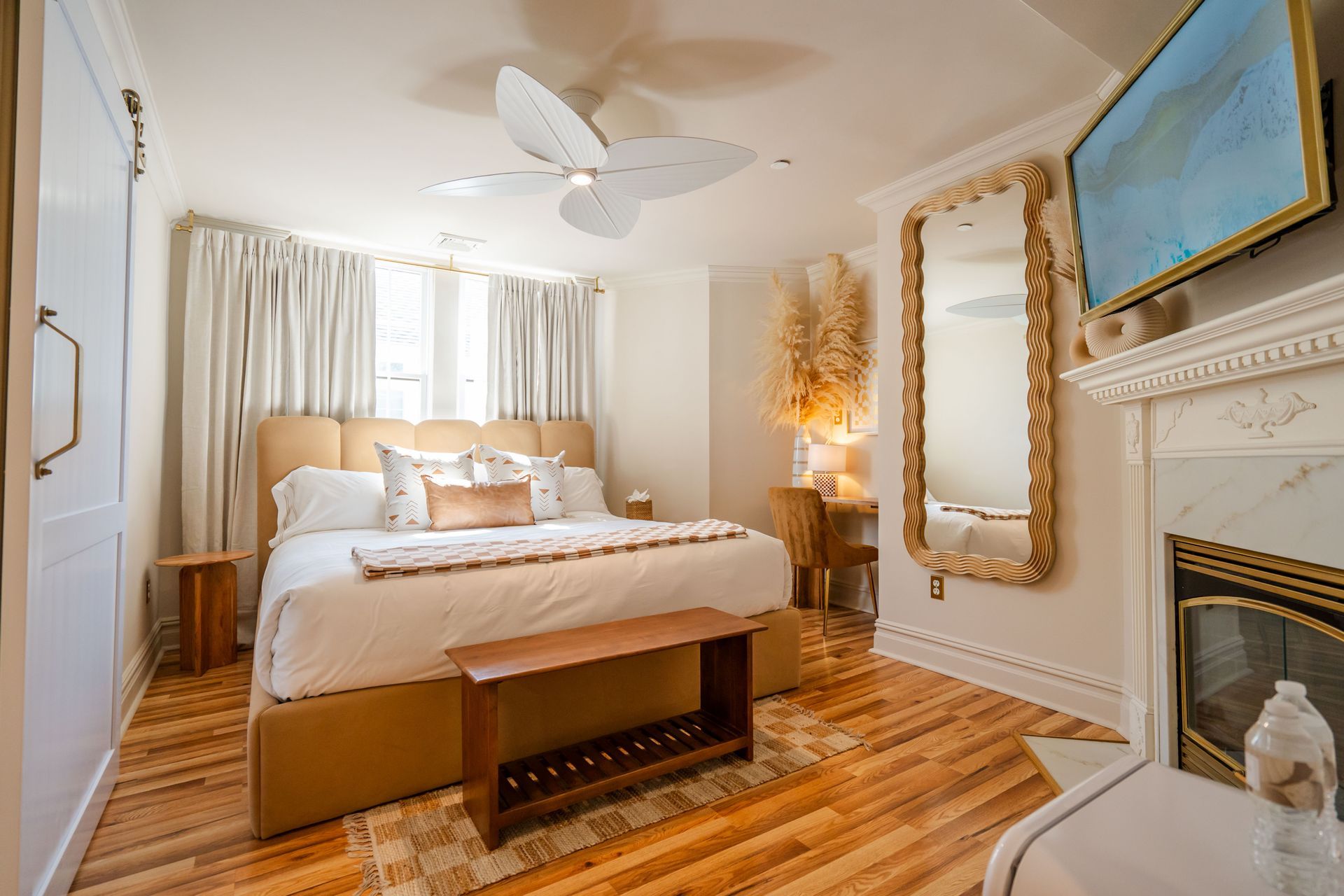 Bedroom with a bed, fireplace, large mirror, and ceiling fan; light color scheme.