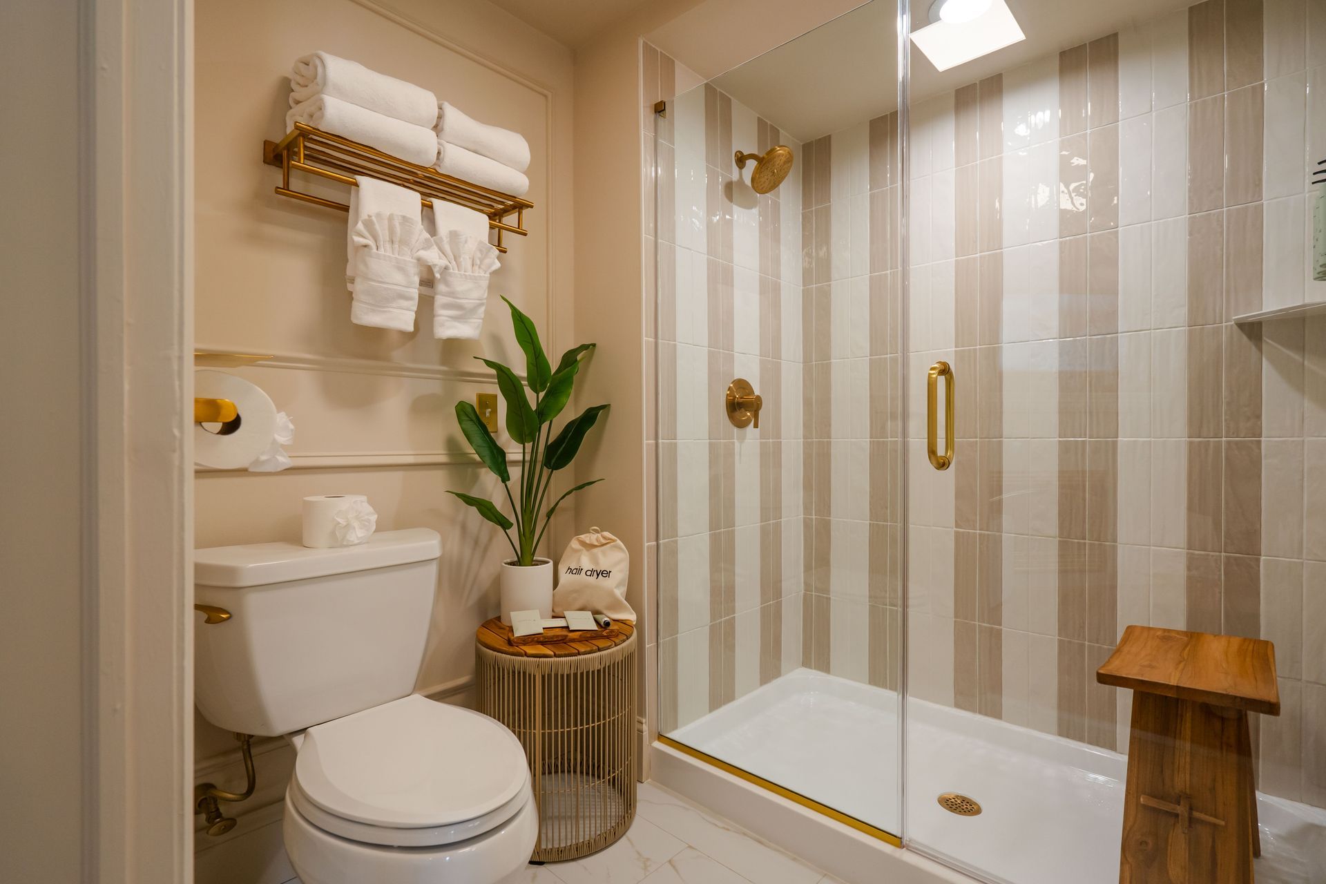 A small, bright bathroom with a toilet, shower, towels, and decorative items.