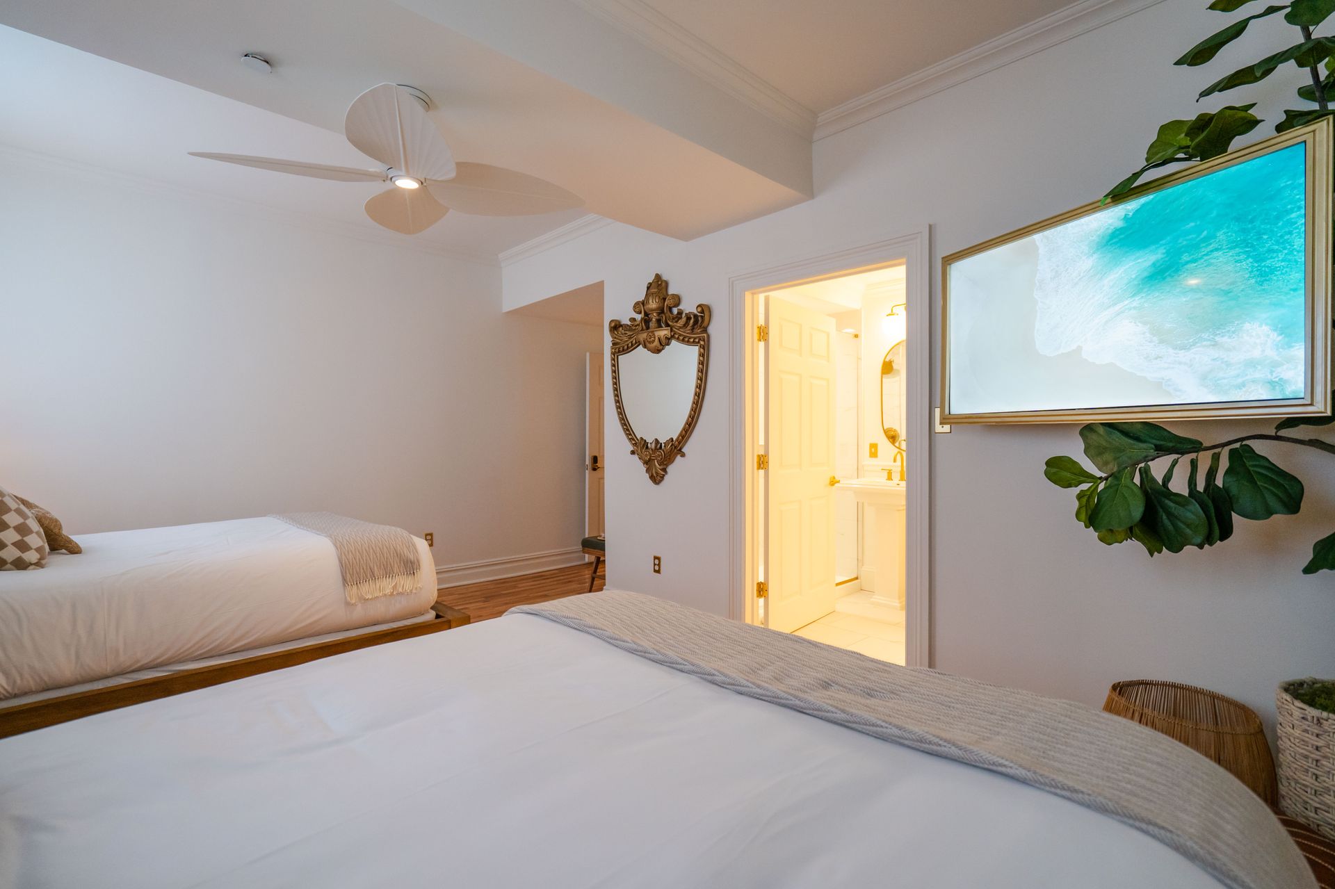 Bedroom with two beds, a mirror, and a TV with a nature scene displayed, with a plant.