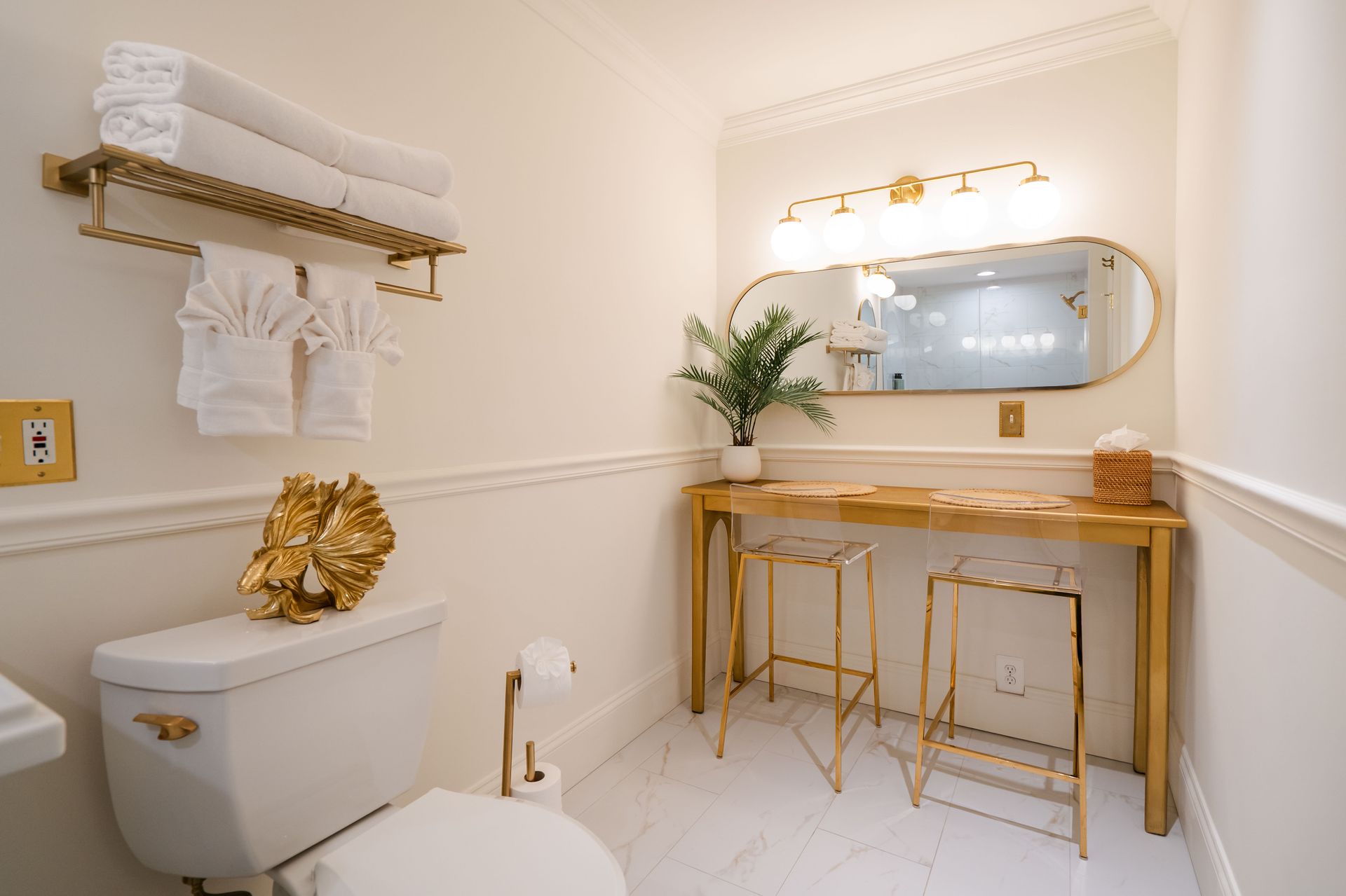 Elegant white bathroom with gold accents: vanity, toilet, towel rack, and mirror.