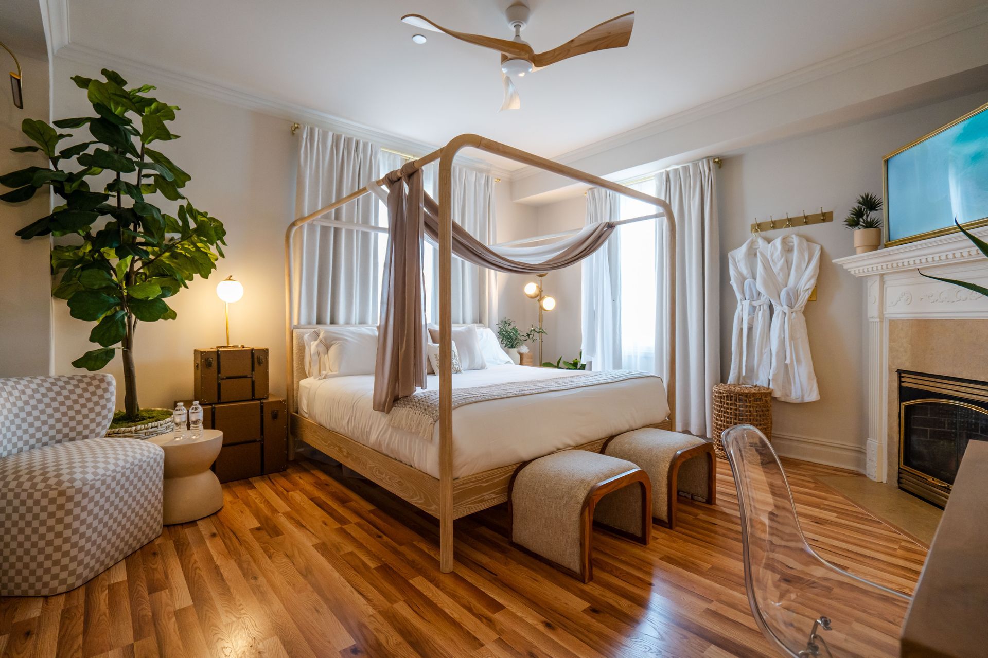 Bedroom with canopy bed, hardwood floors, large plant, fireplace, and neutral tones.