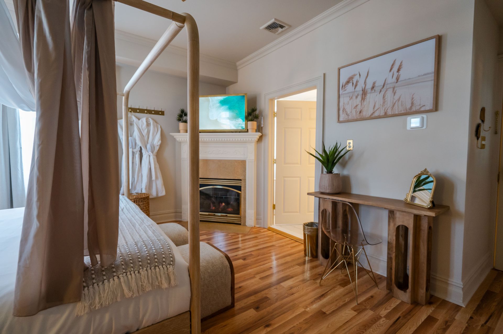 Bedroom with canopy bed, fireplace, wooden desk, and hardwood floor.