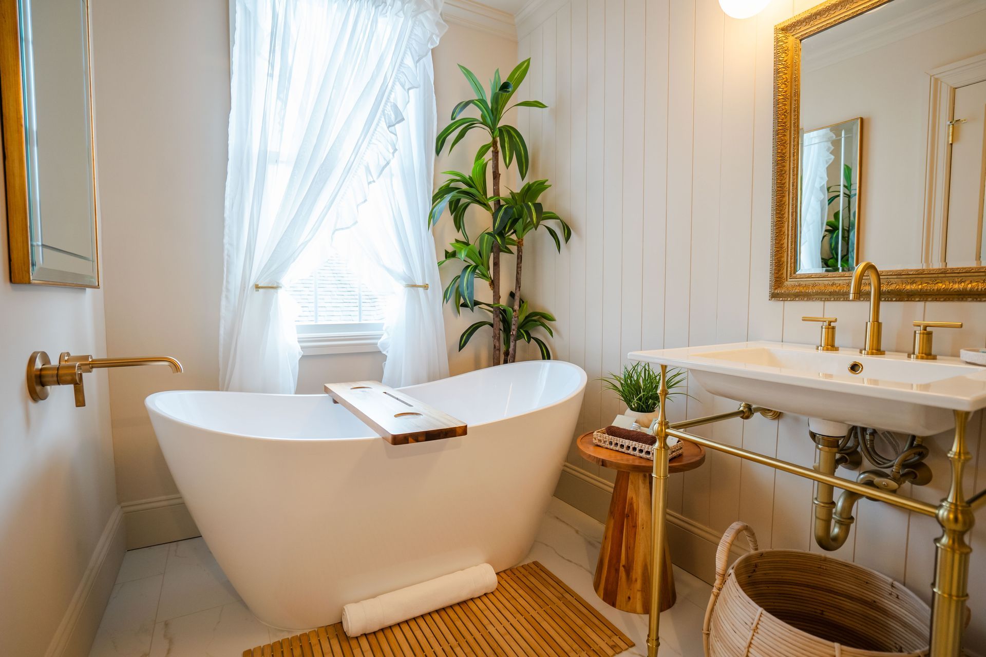 Elegant white bathroom with a freestanding tub, gold fixtures, and a potted plant.