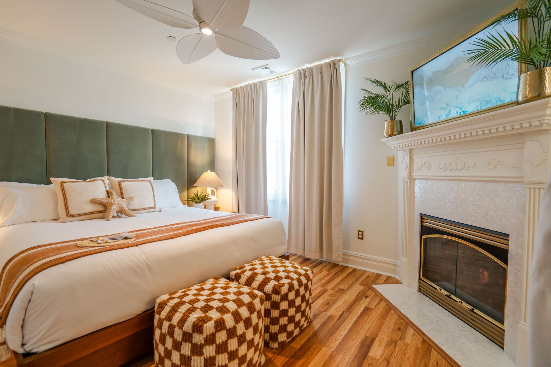 Bedroom with large bed, fireplace, and patterned ottomans.