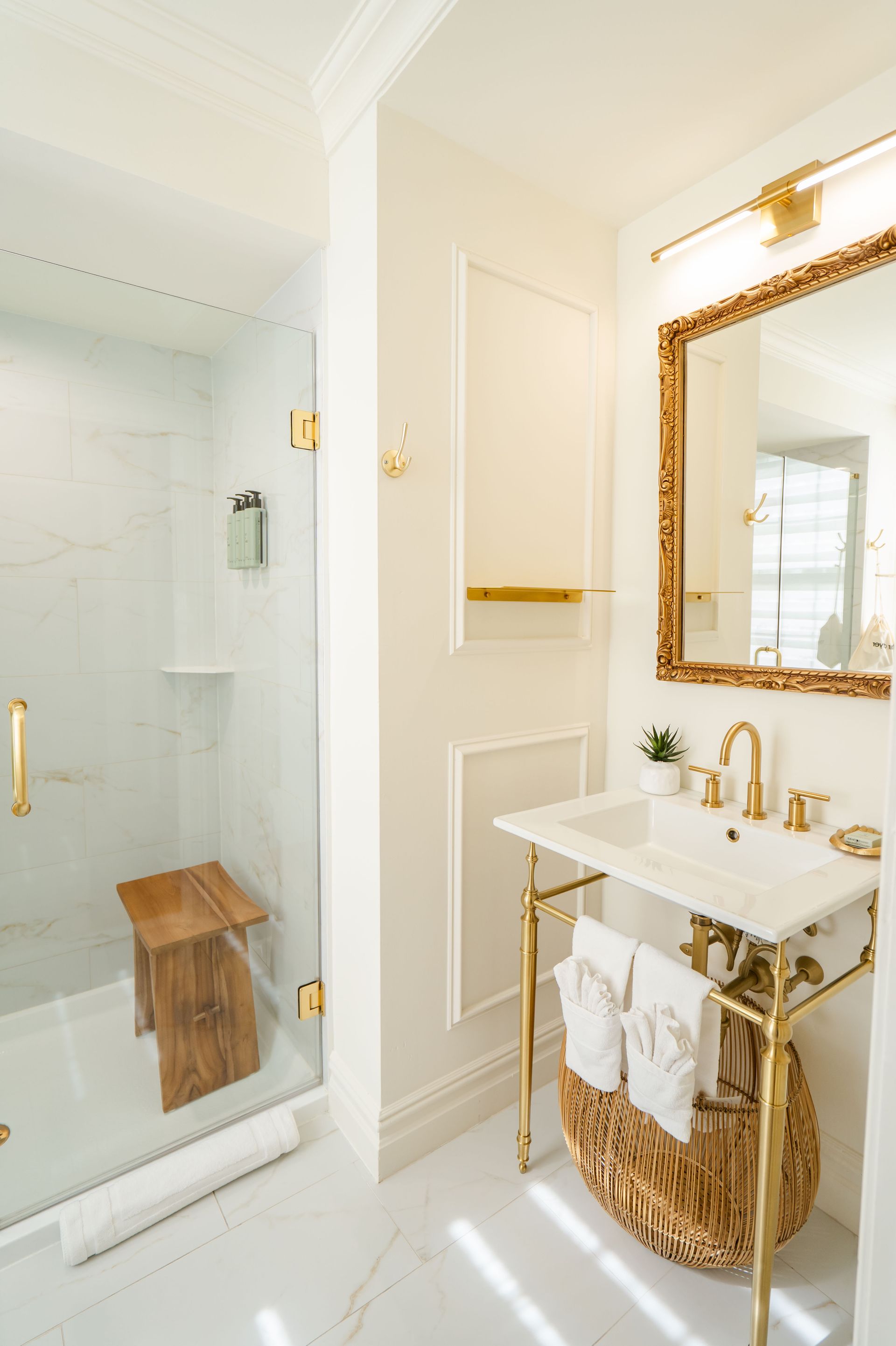 Elegant white bathroom with gold accents. Includes a glass shower, marble sink, and ornate mirror.