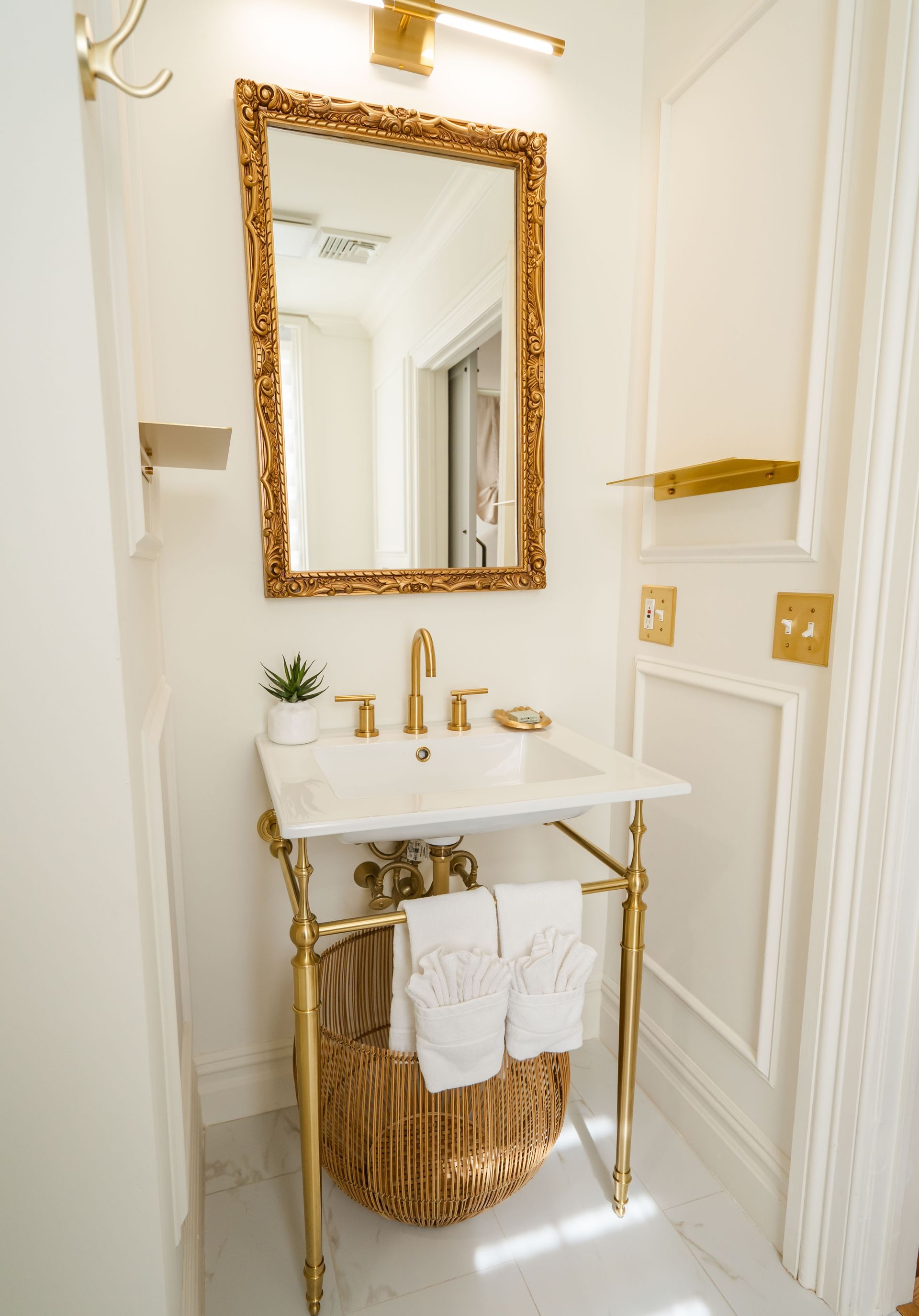 Bathroom with a gold-framed mirror, gold fixtures, marble sink, and woven basket below.