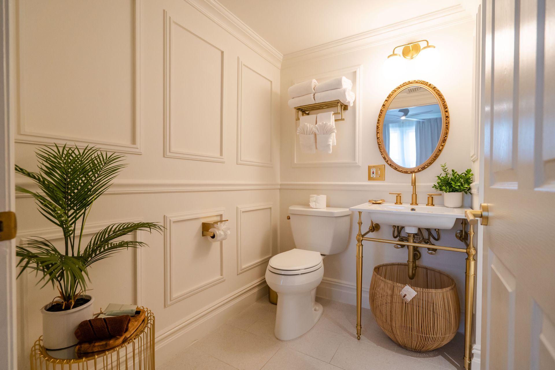 Elegant white bathroom with gold accents, including sink, mirror, towel rack, and decorative paneling.