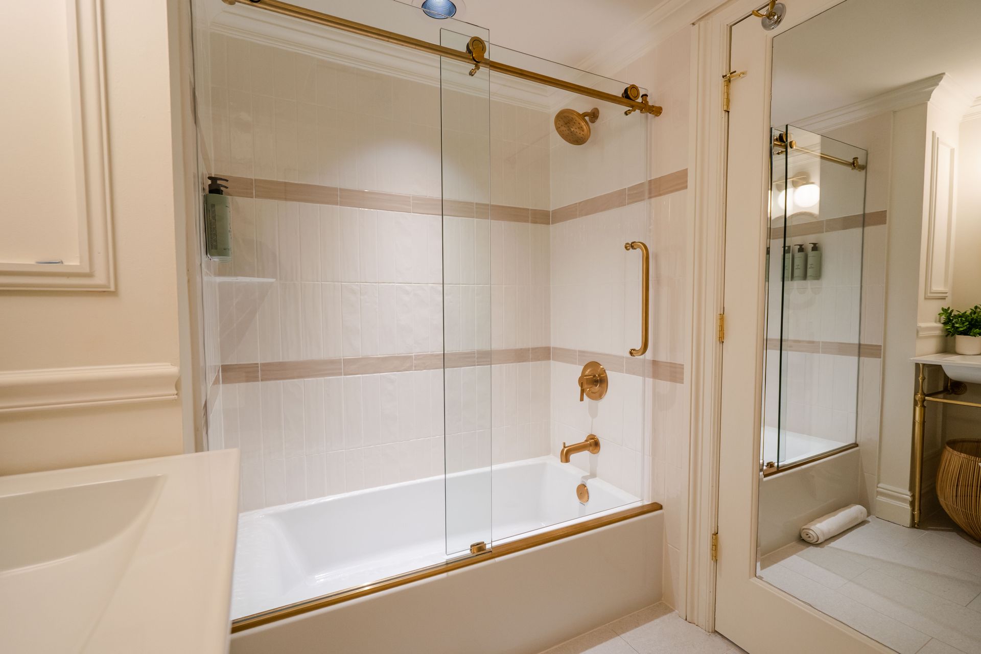 Bathroom with white tile, gold fixtures, glass shower door, and a tub.