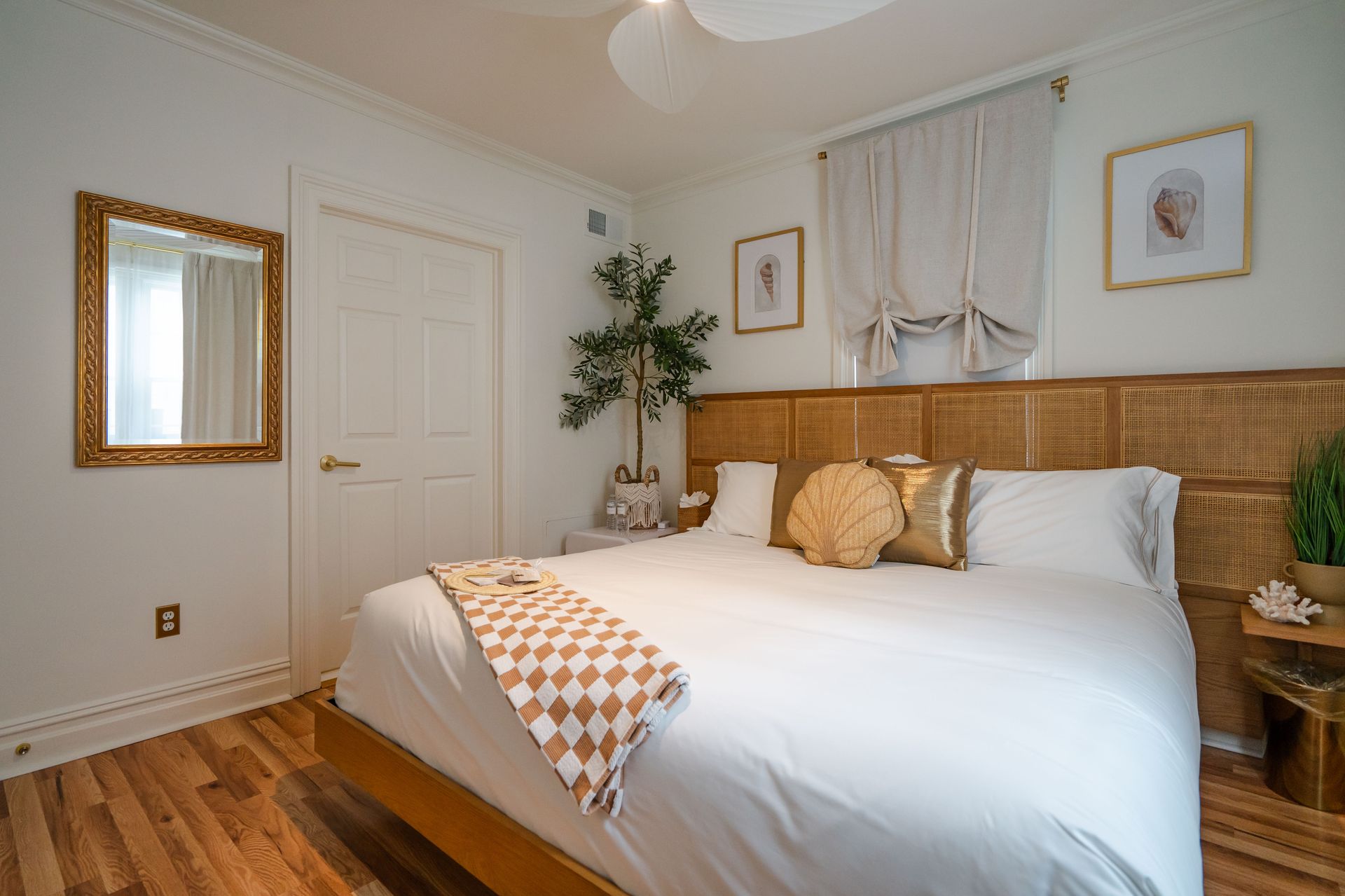 Bedroom with a wooden headboard, gold accents, white bedding, and hardwood floors.