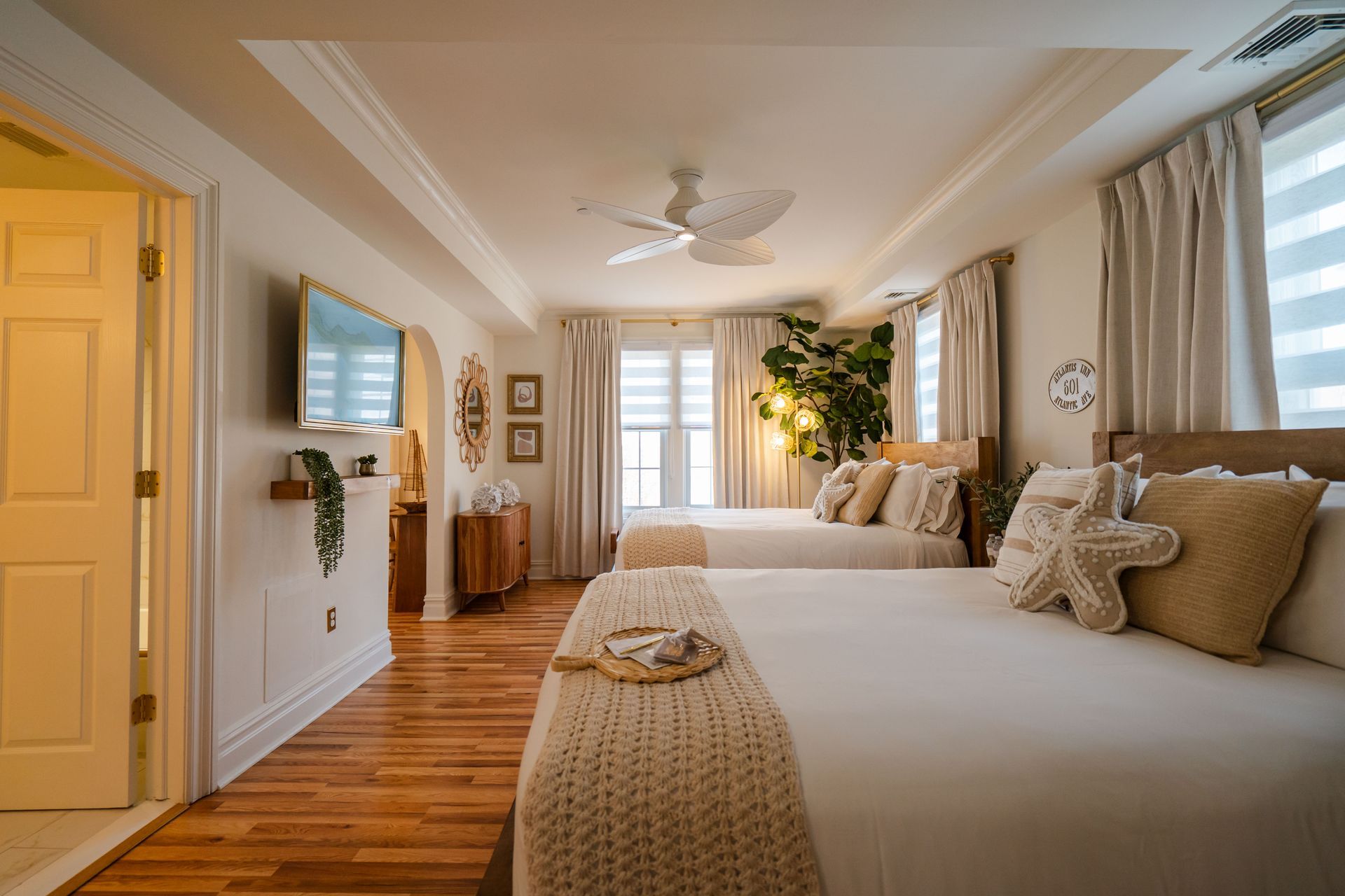 Bedroom with two beds, white walls, wooden floors, and a ceiling fan.