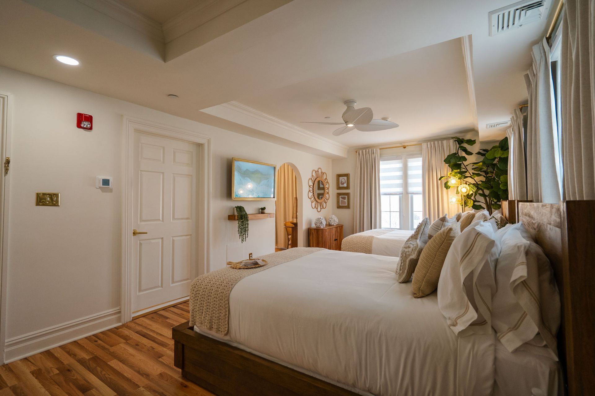 Bedroom with two beds, white walls, wooden floors, and a ceiling fan.
