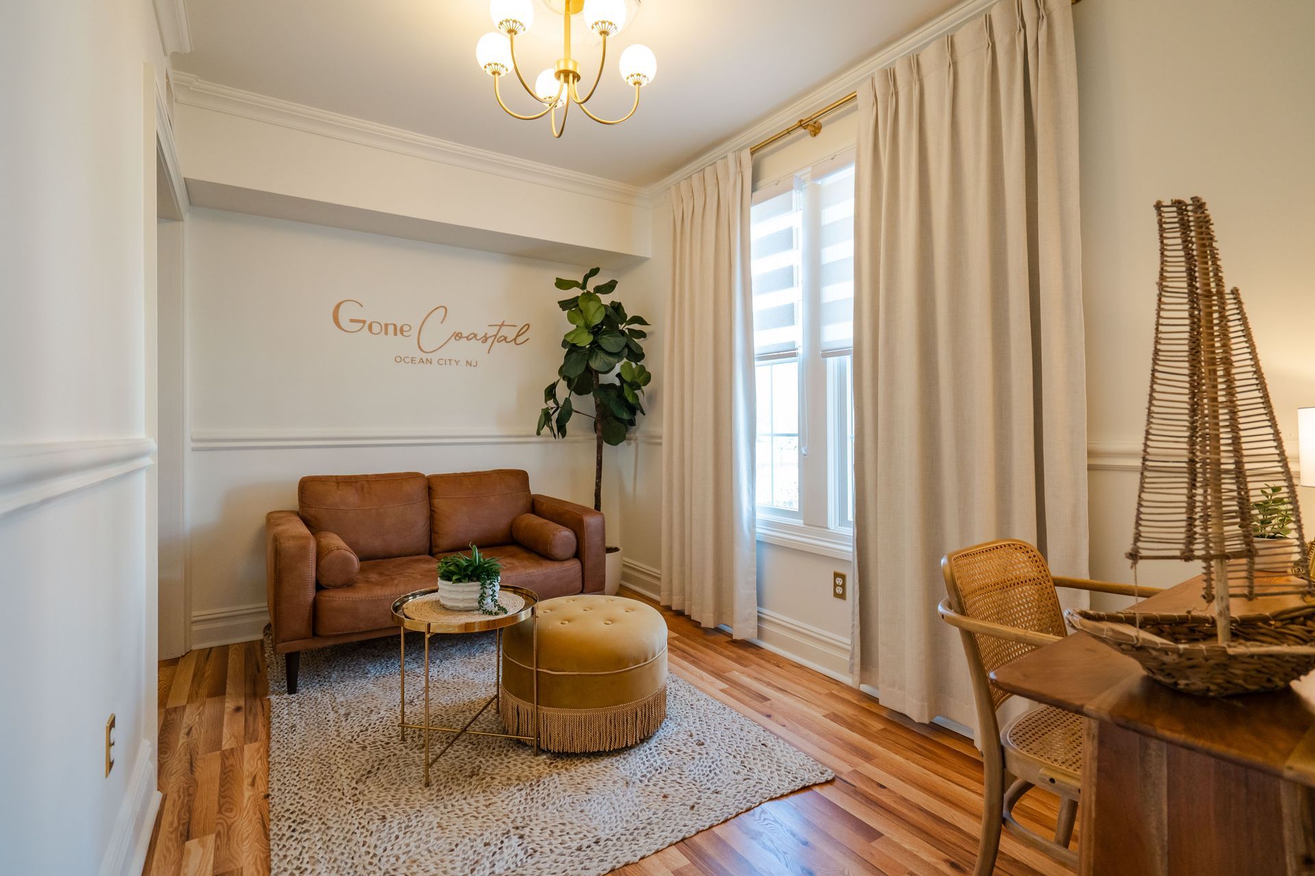 Cozy room with brown sofa, fringed ottoman, and decorative ship near window with drapes.