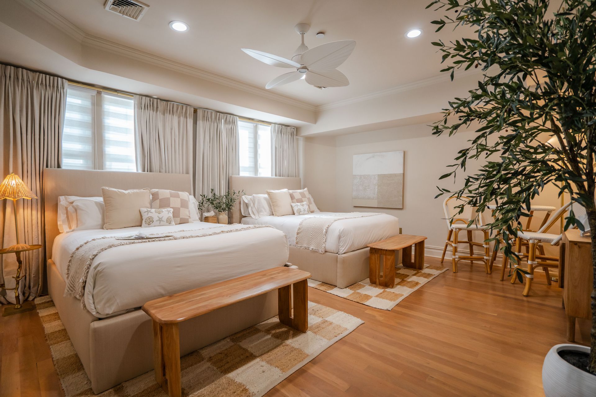 Bedroom with two beds, neutral tones. Wooden benches, rug, and faux tree.
