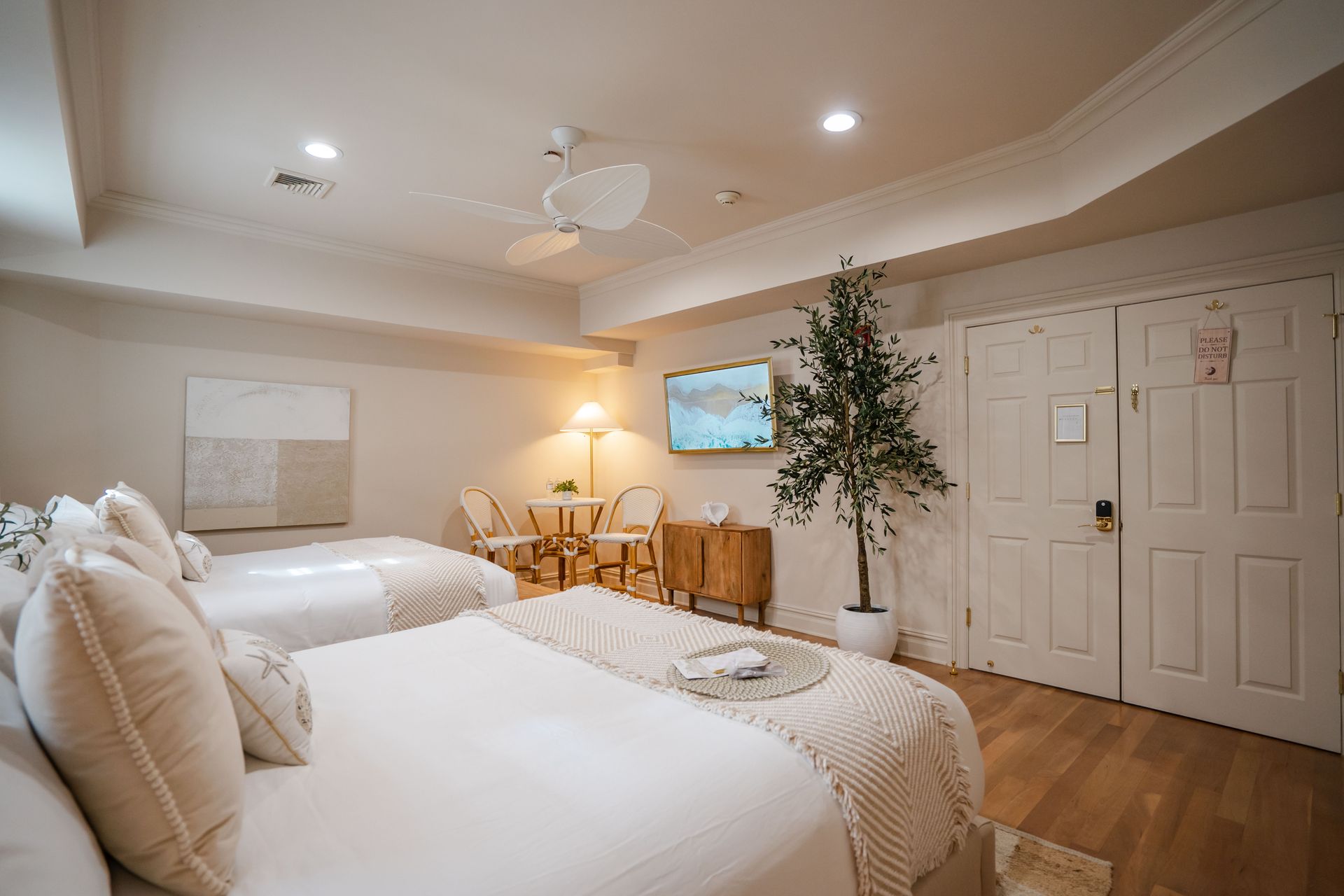 Bedroom with two beds, neutral tones, wood floors, and decorative tree.