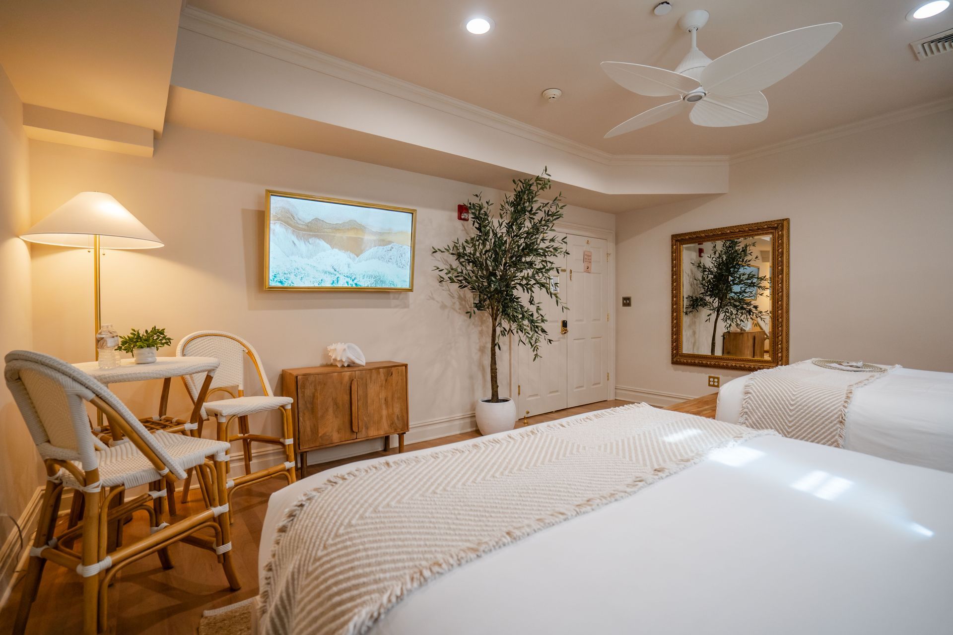 Spa room with two beds, small table and chairs, olive tree, TV, and mirror.