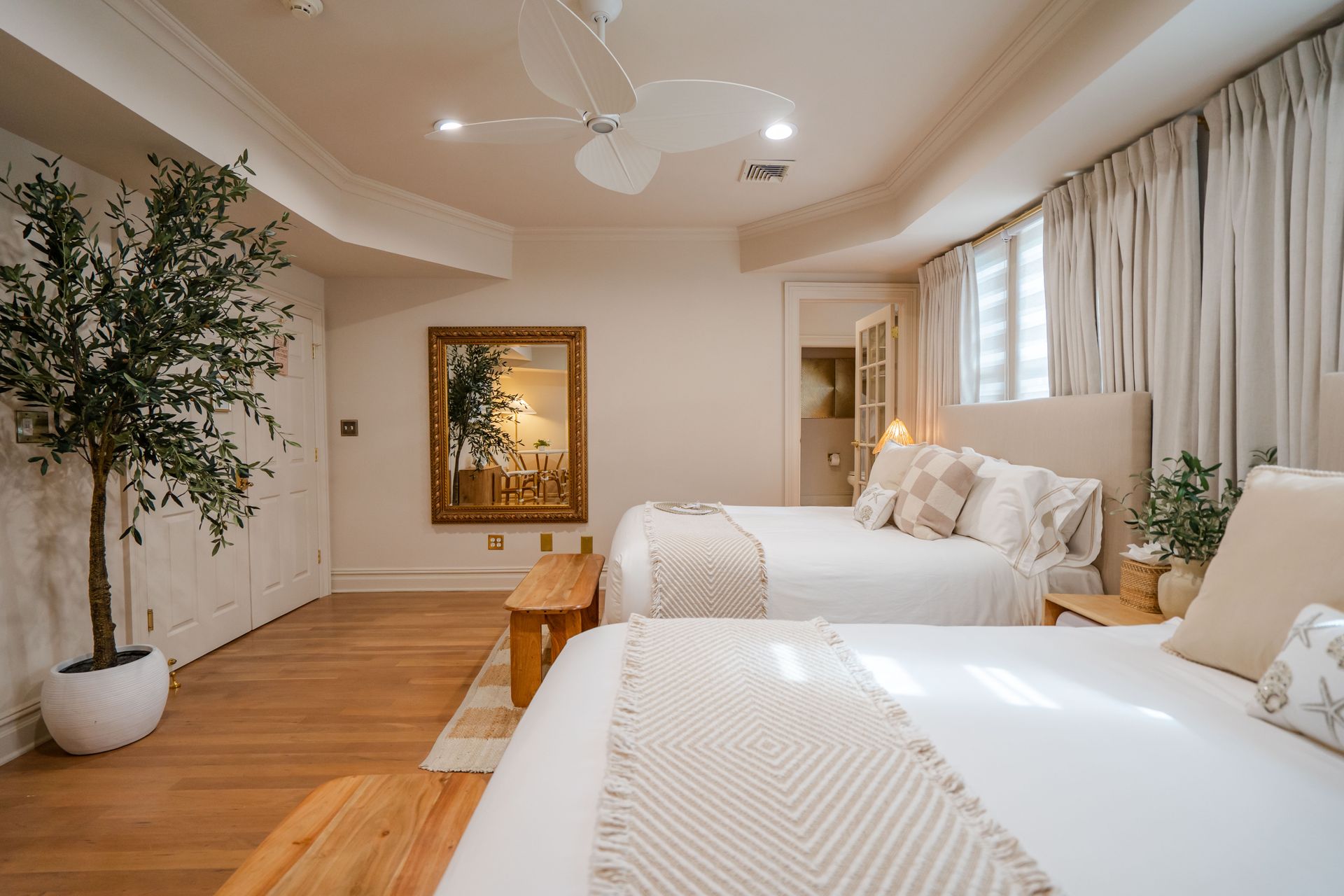 Bedroom with two beds, wooden floors, a large mirror, and a potted tree.