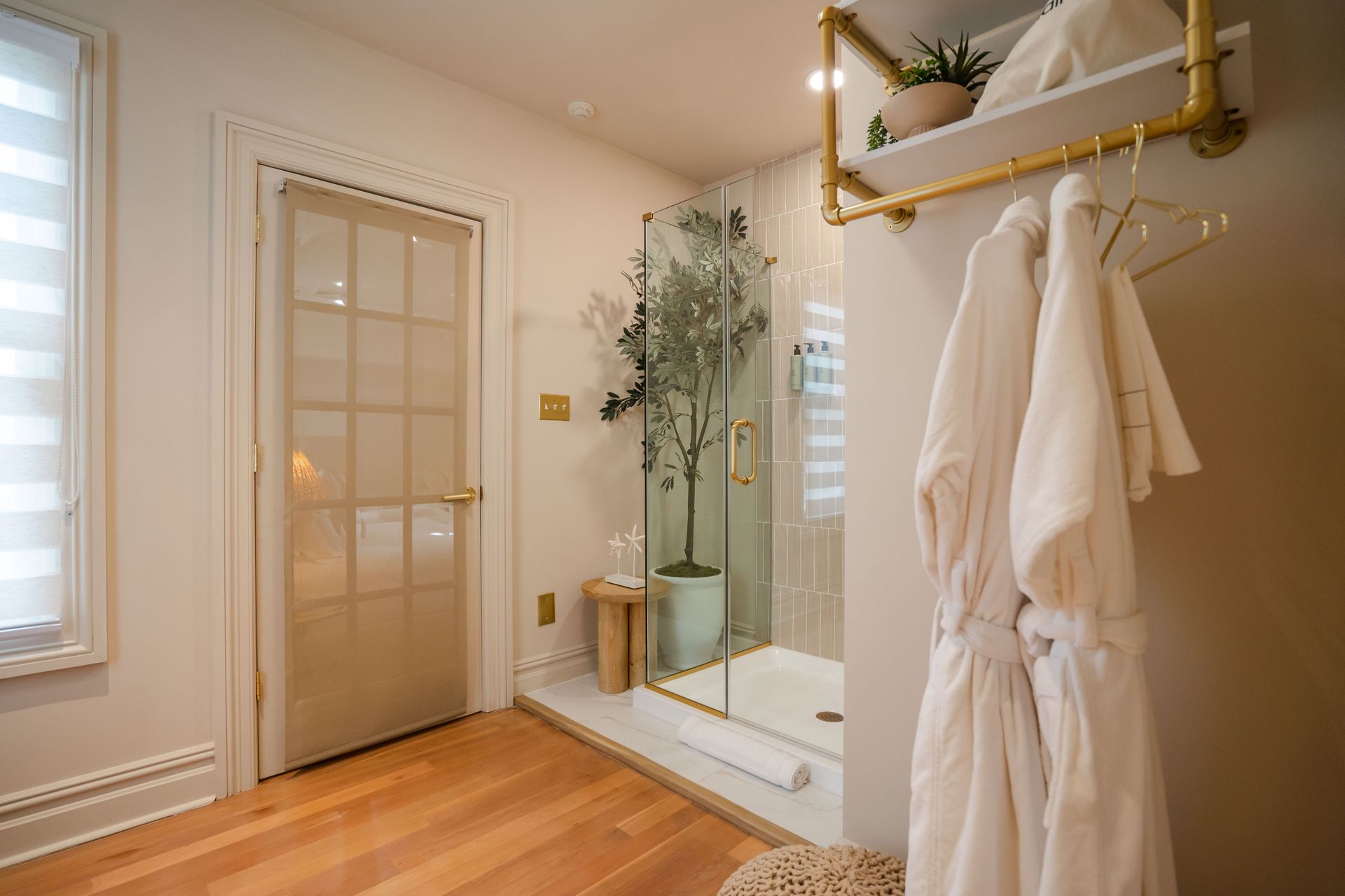 Bathroom with glass shower, robe on rack, door, wood floor, and gold accents.
