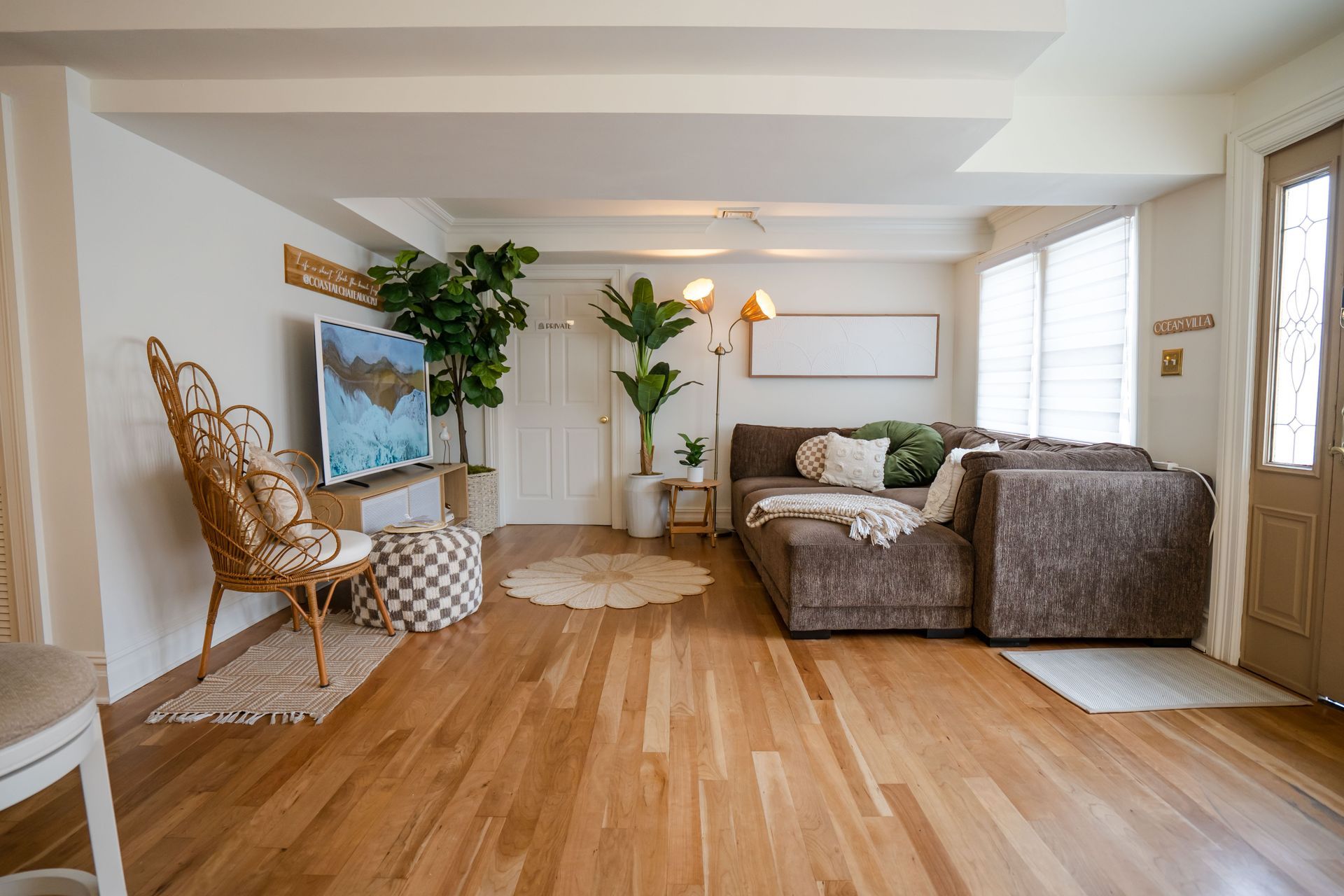 Living room with brown sectional sofa, hardwood floors, plants, and natural light.