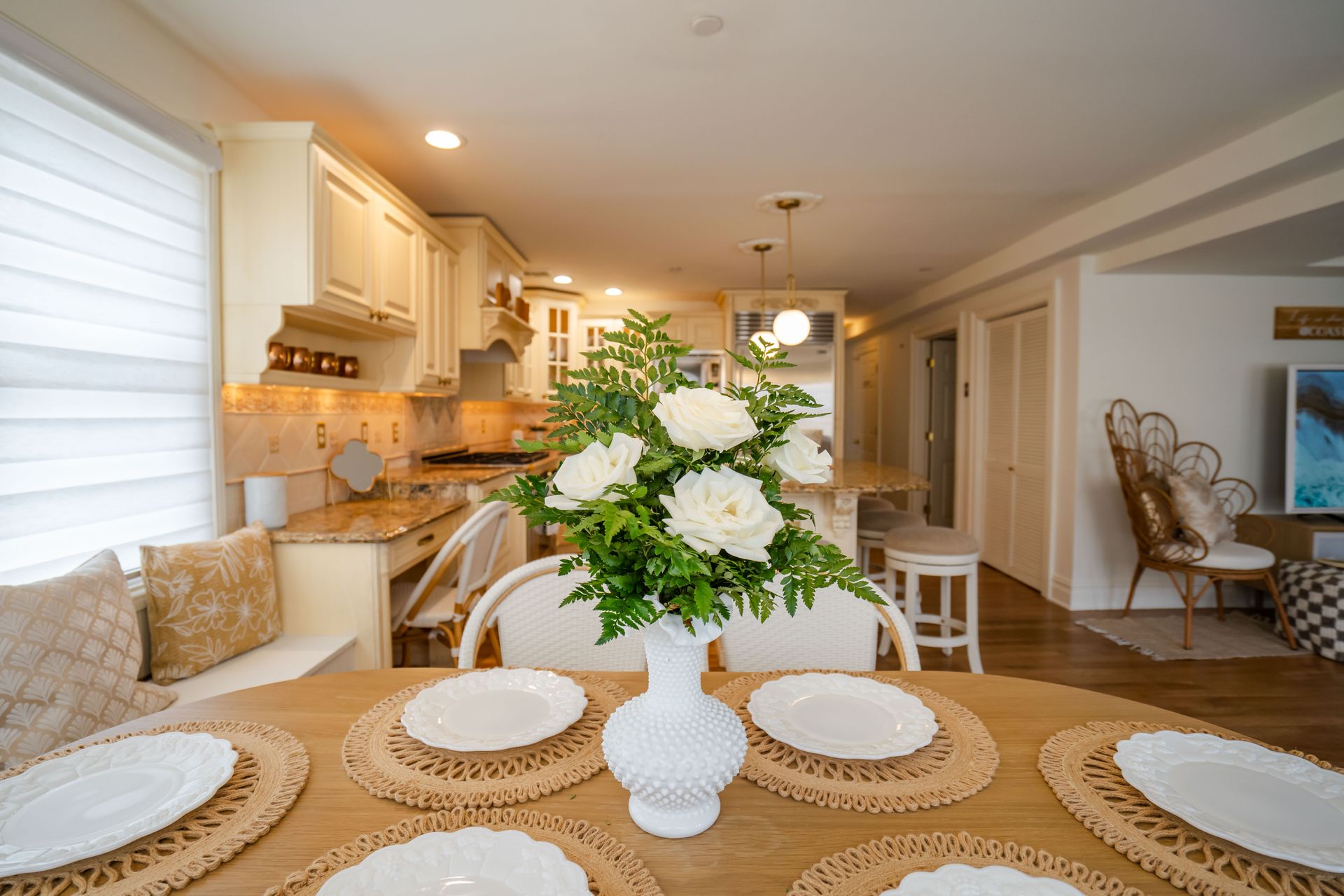 Dining table set with plates and flowers, leading to an open kitchen with creamy cabinetry.