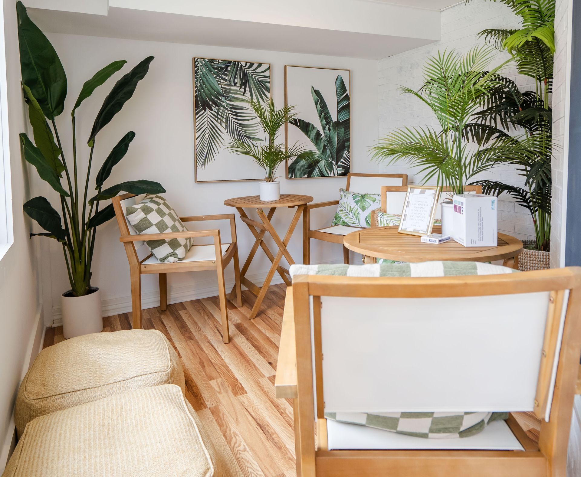 Cozy outdoor seating area with wooden chairs, small table, plants, and art on white walls.