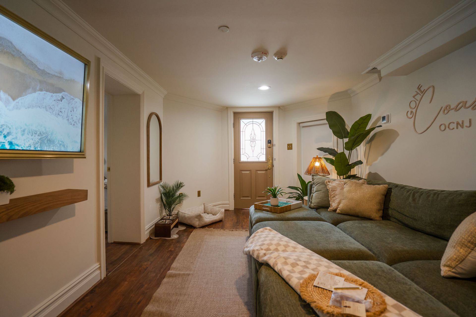 Cozy living room with green sectional sofa, doorway, TV, and decorative plants.