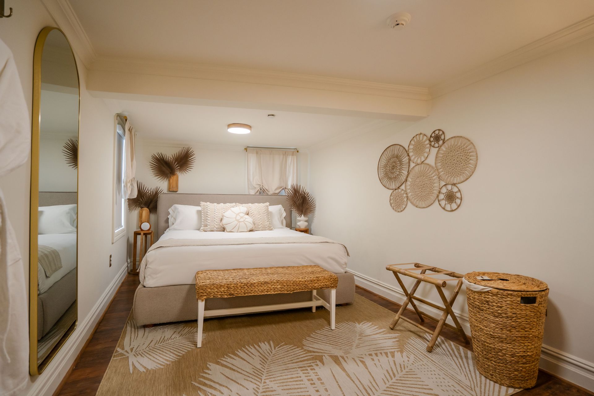 Bedroom with neutral tones, bed, rug, mirror, and wicker accents.