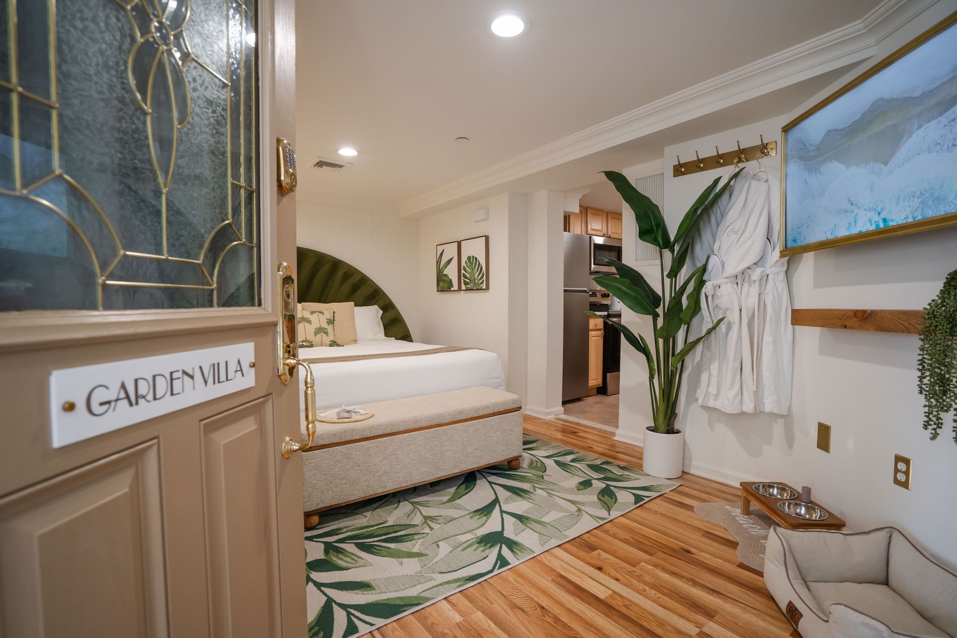 Cozy villa entrance with open door, bed, green rug, and live plants.