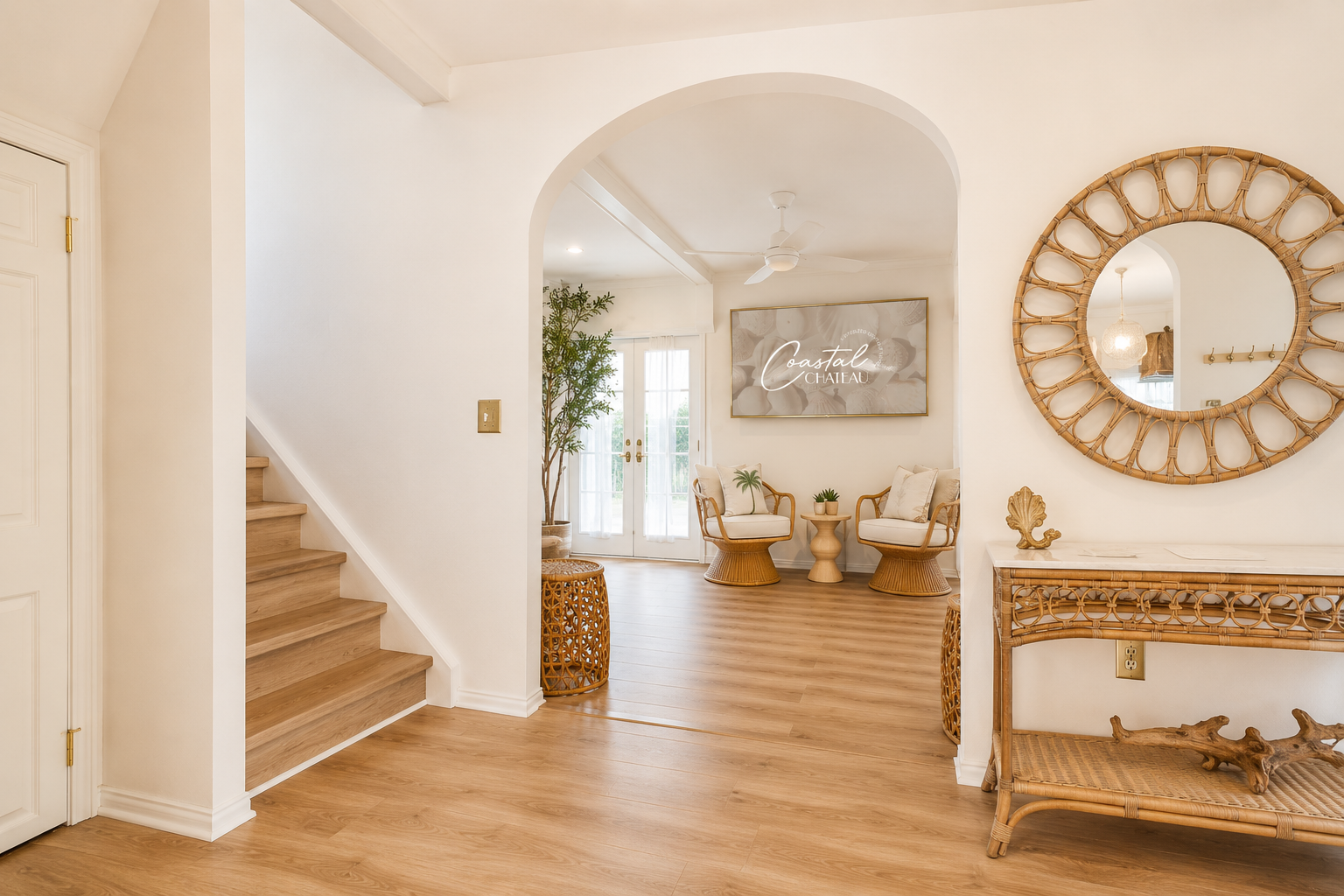 Bright entry hall with wood floors, staircase, arched doorway, and a round mirror above a console table.