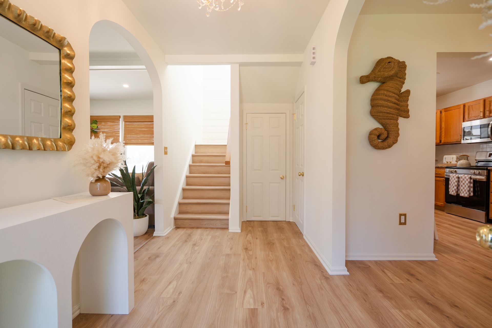 Bright entryway with arched openings, staircase, wood floors, and a seahorse wall decor in a beige home