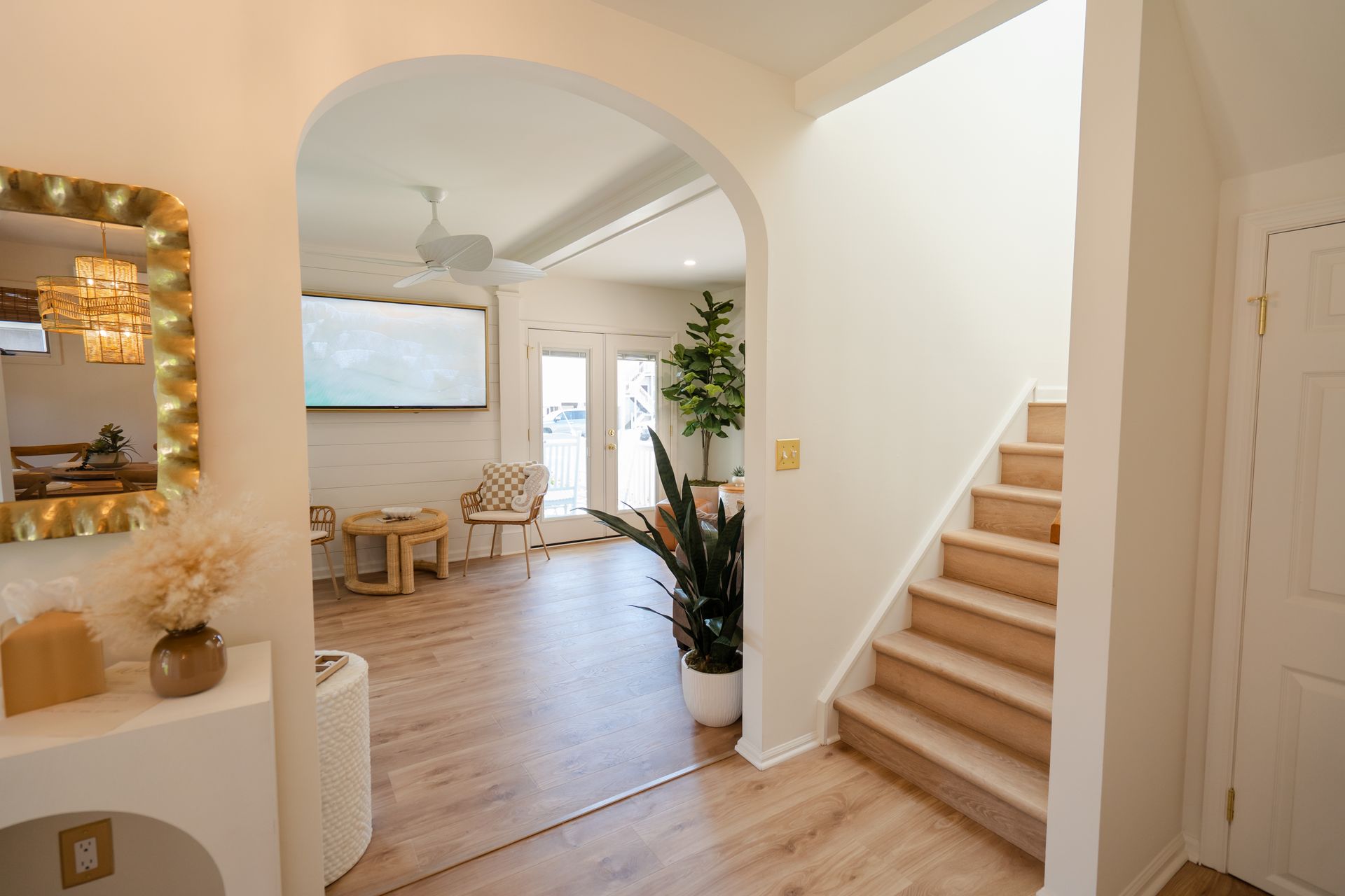 Bright entryway with arched opening, staircase, and a sunlit living area with light wood floors