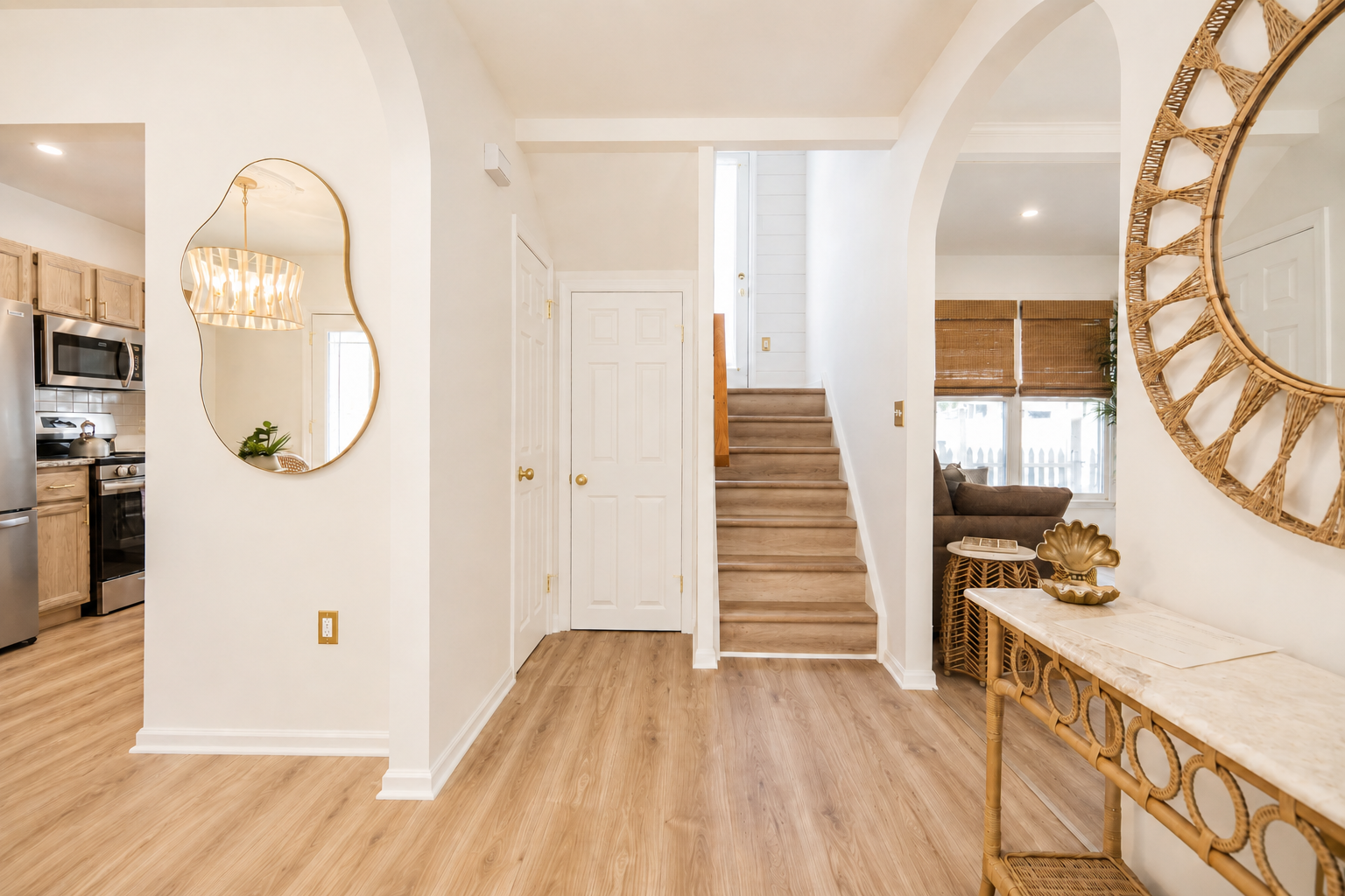 Bright foyer with wood floors, staircase, gold-framed mirror, and a glimpse of the kitchen and dining area.
