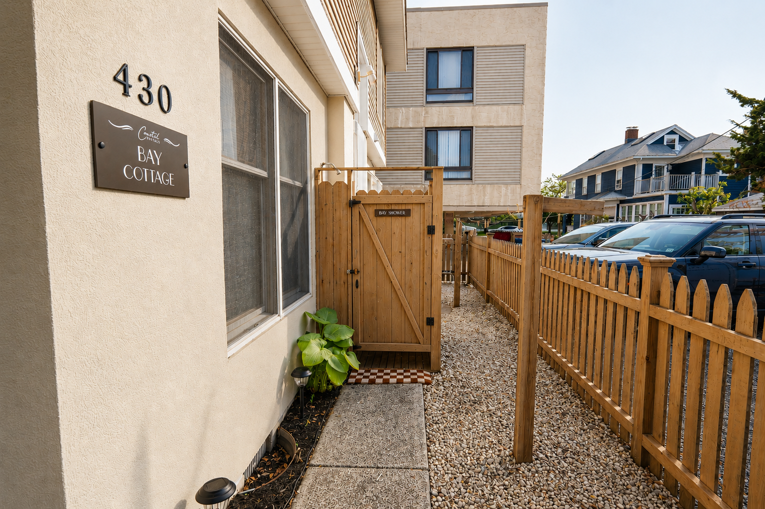 Narrow gravel side yard with wooden gate, fence, parked cars, and apartment building entrance number 430.