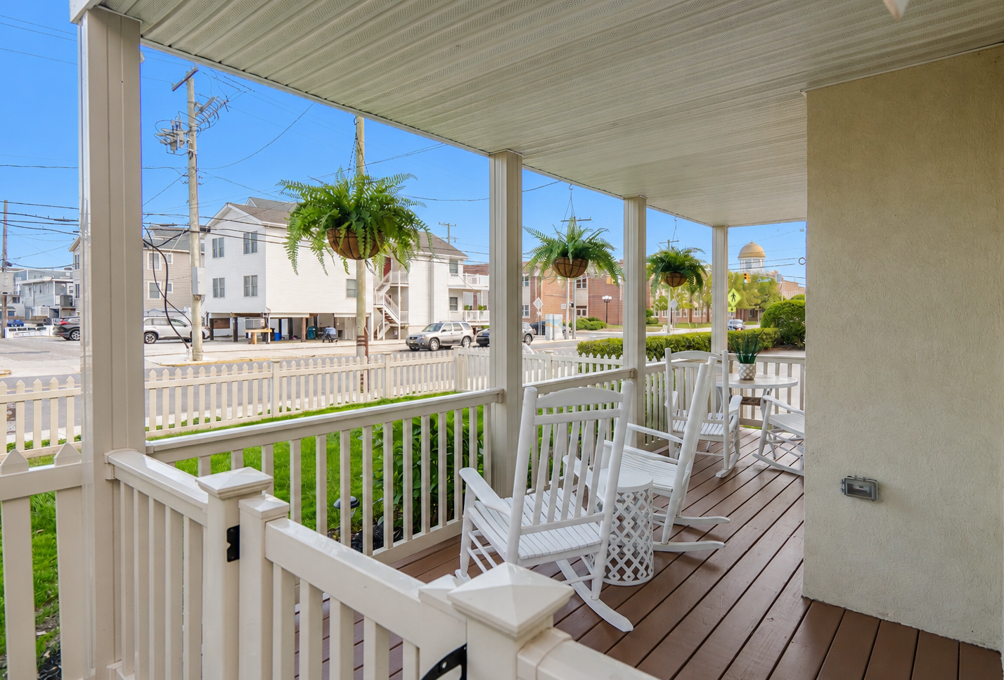 Front porch with white rocking chairs, hanging ferns, and a view of a quiet suburban street