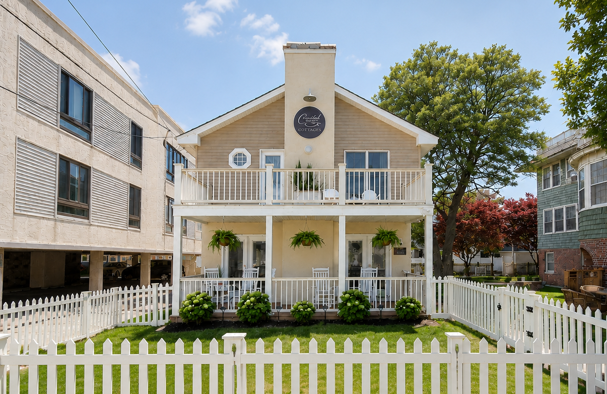 White two-story house with balcony, clock tower, and picket fence in a landscaped yard