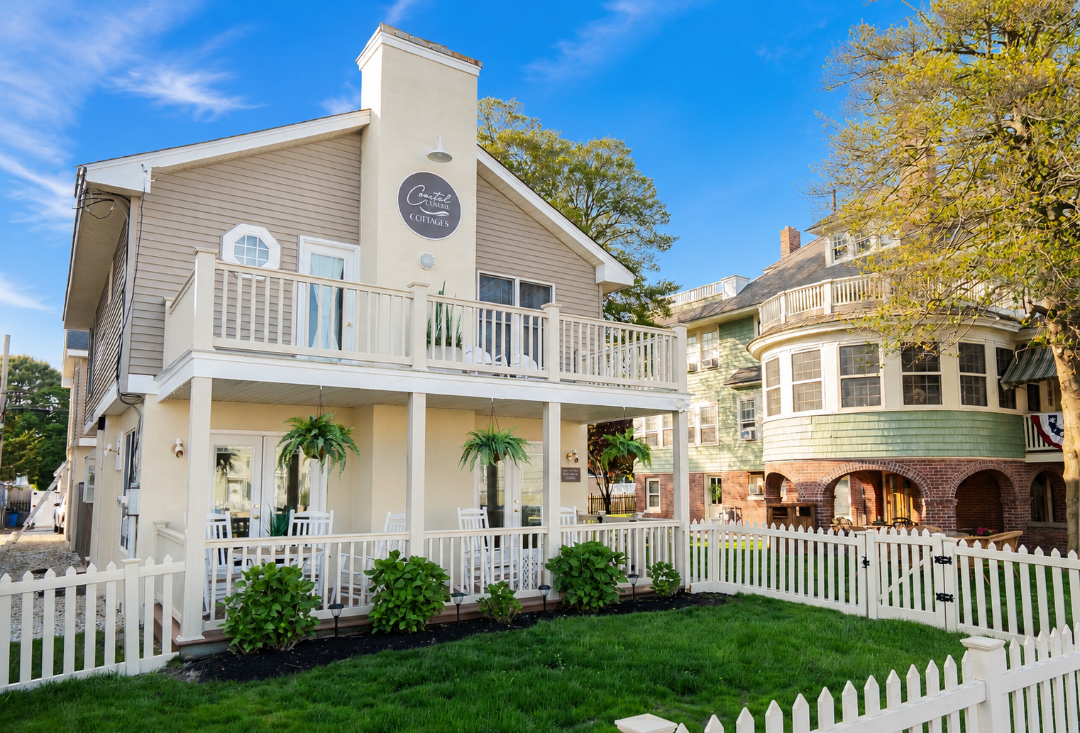 Victorian-style white house with a balcony, clock tower, and picket fence on a sunny street