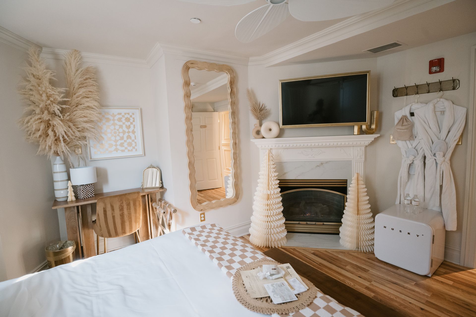 Bedroom with bed, fireplace, large mirror, and decorative accents in neutral tones.