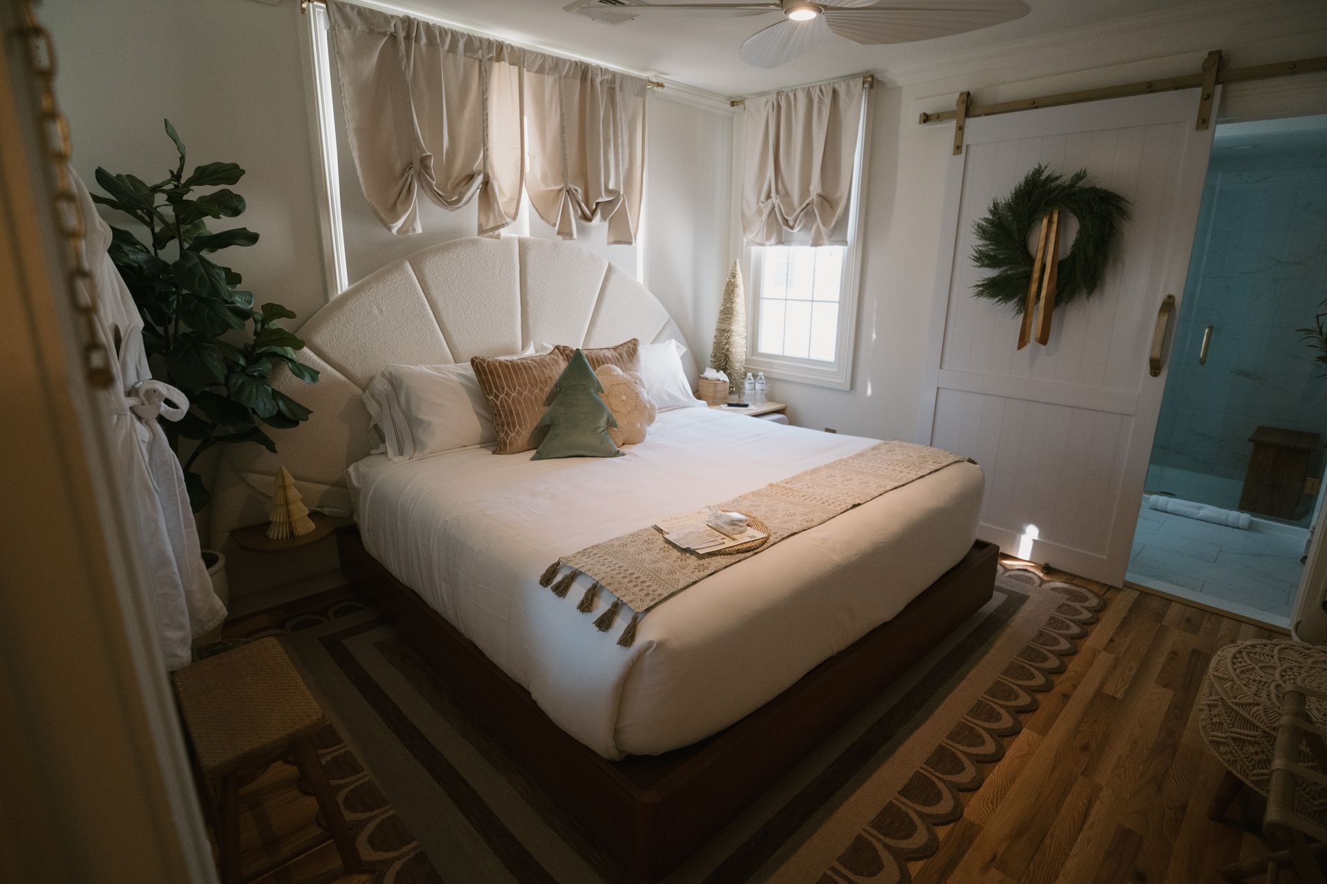 Cozy bedroom with white bed, beige curtains, and open door to a bathroom. Decorated for the holidays.