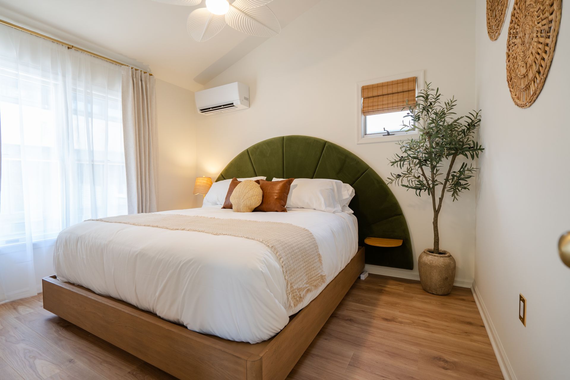 Cozy bedroom with a low bed, white bedding, green arch headboard, and warm wood floors