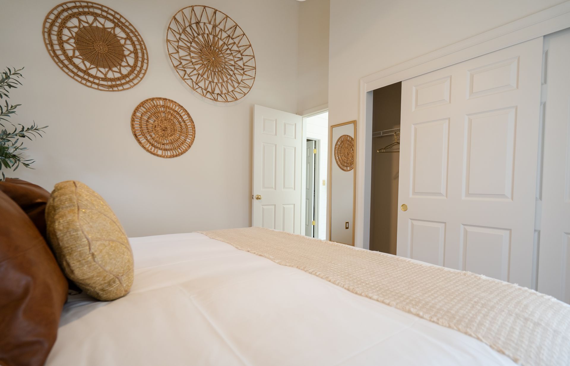 Bedroom with a bed, woven wall decor, white closet doors, and a mirror near an open doorway