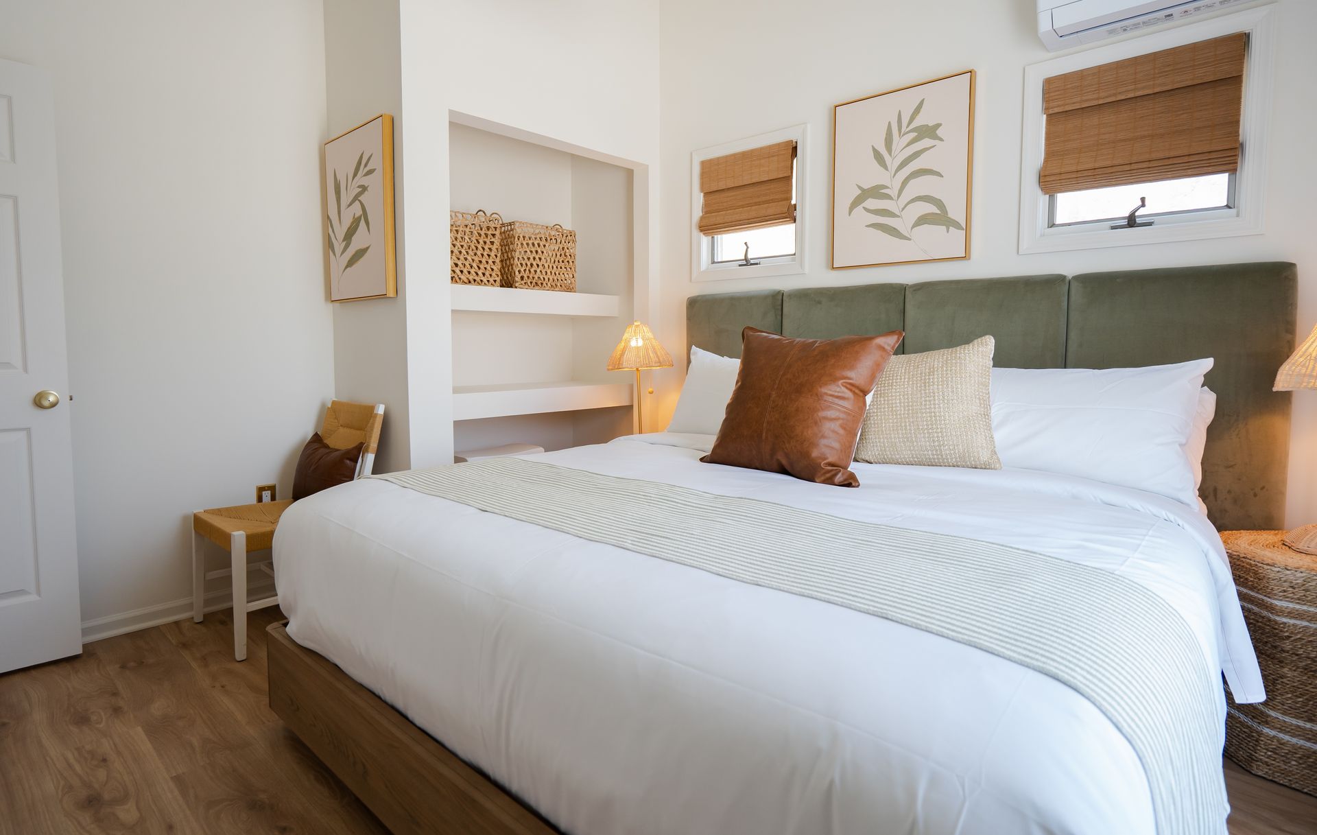 Bright bedroom with white bedding, green headboard, wood floors, and woven window shades