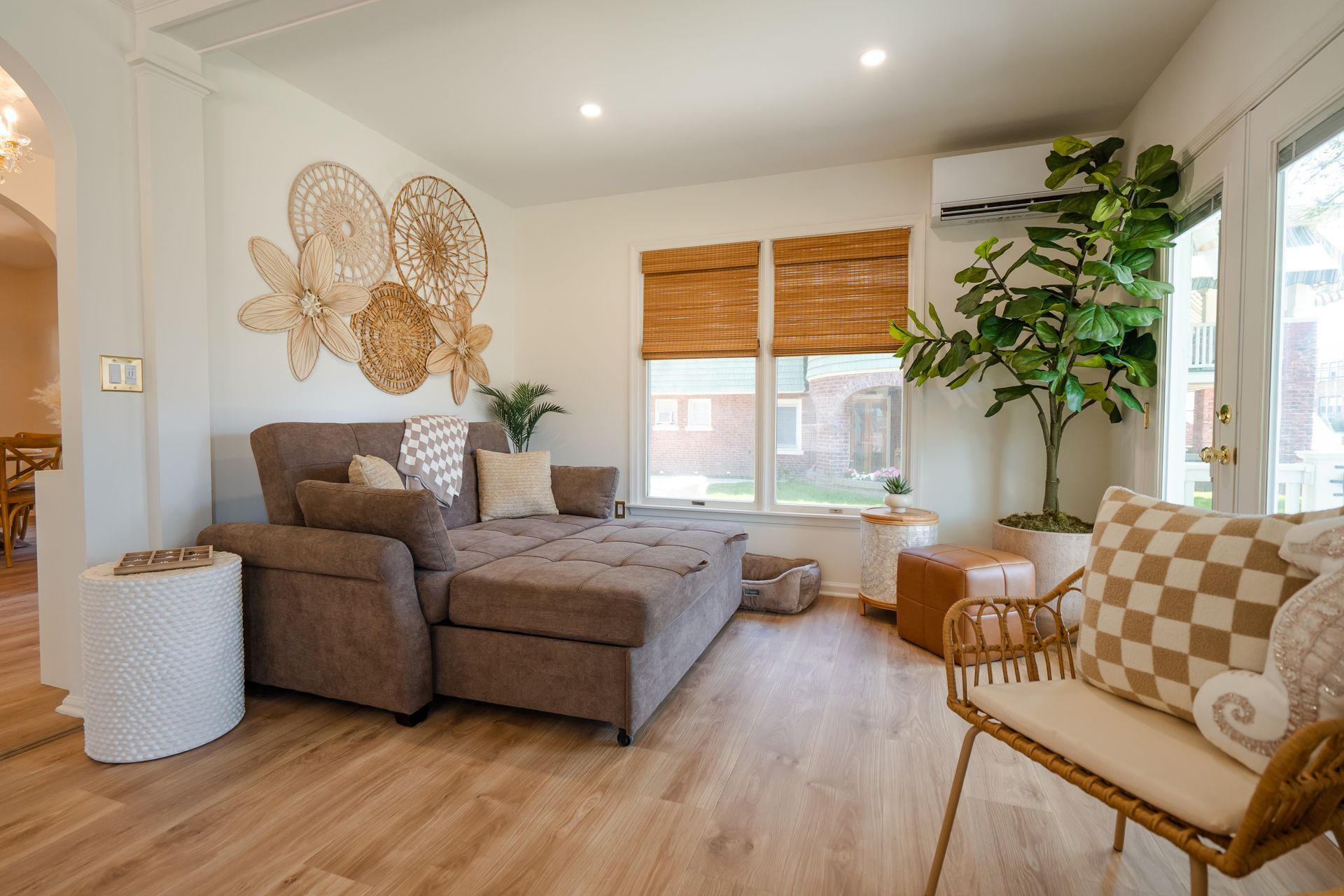 Bright living room with a gray sofa, woven wall decor, plants, and a wicker chair by the window.