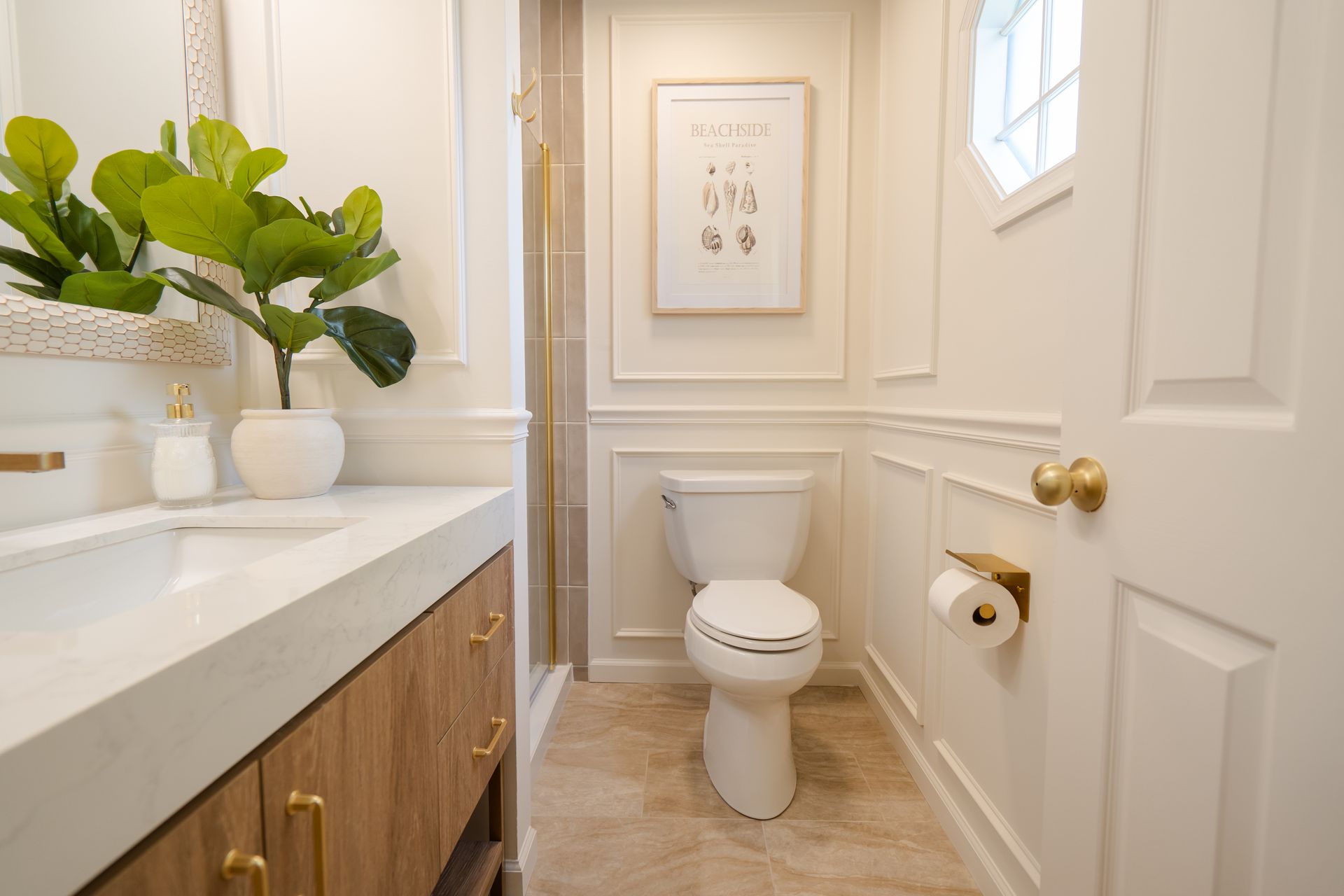 Bright modern bathroom with white vanity, toilet, gold fixtures, and potted plant on the counter