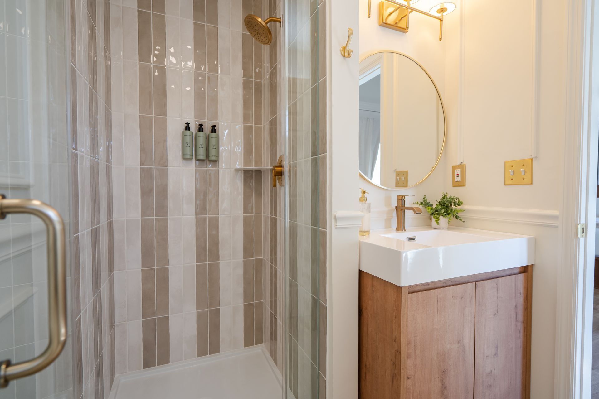 Elegant bathroom with glass shower, striped tile, vanity sink, and round mirror