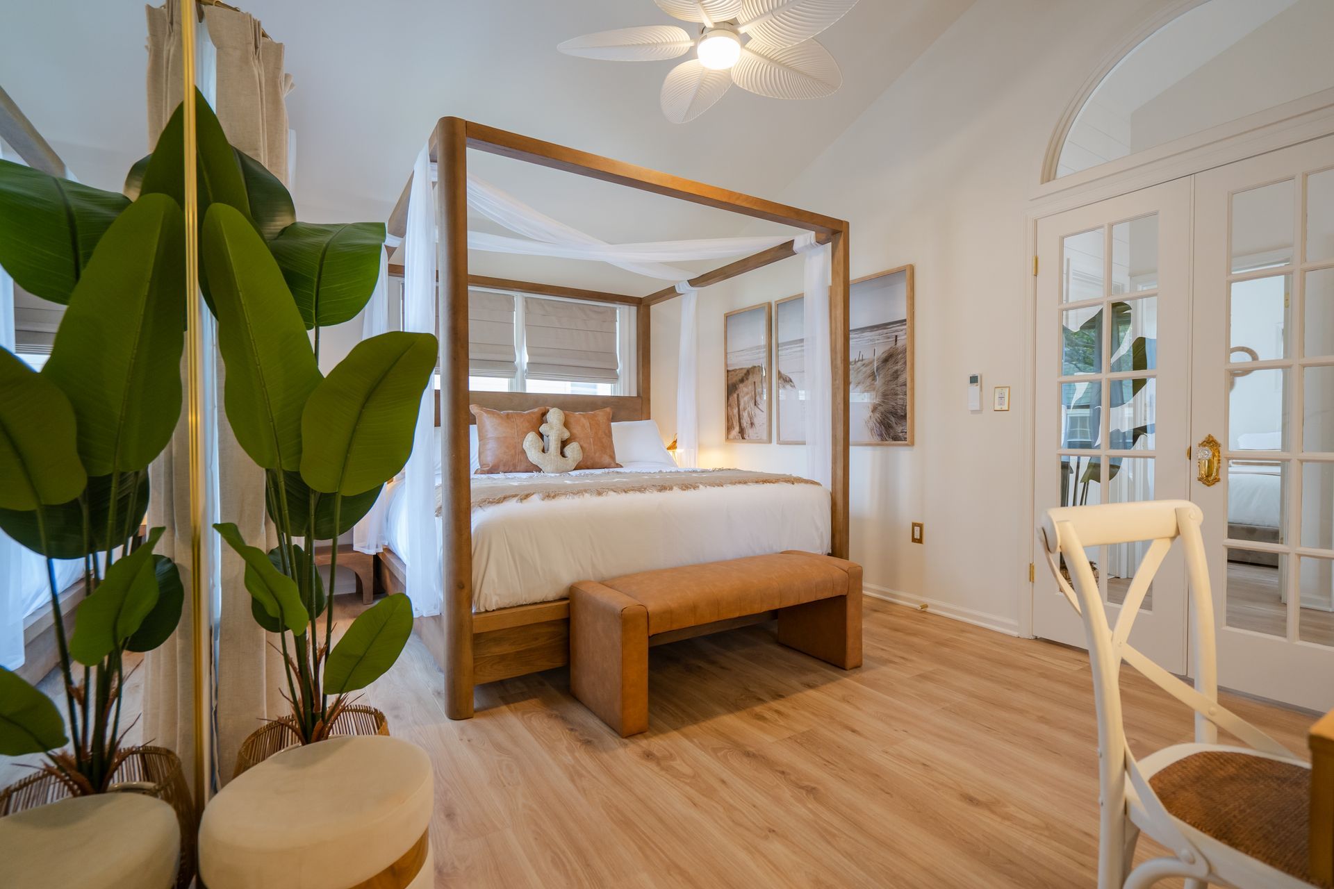Bright bedroom with canopy bed, wooden bench, large plant, and white French doors