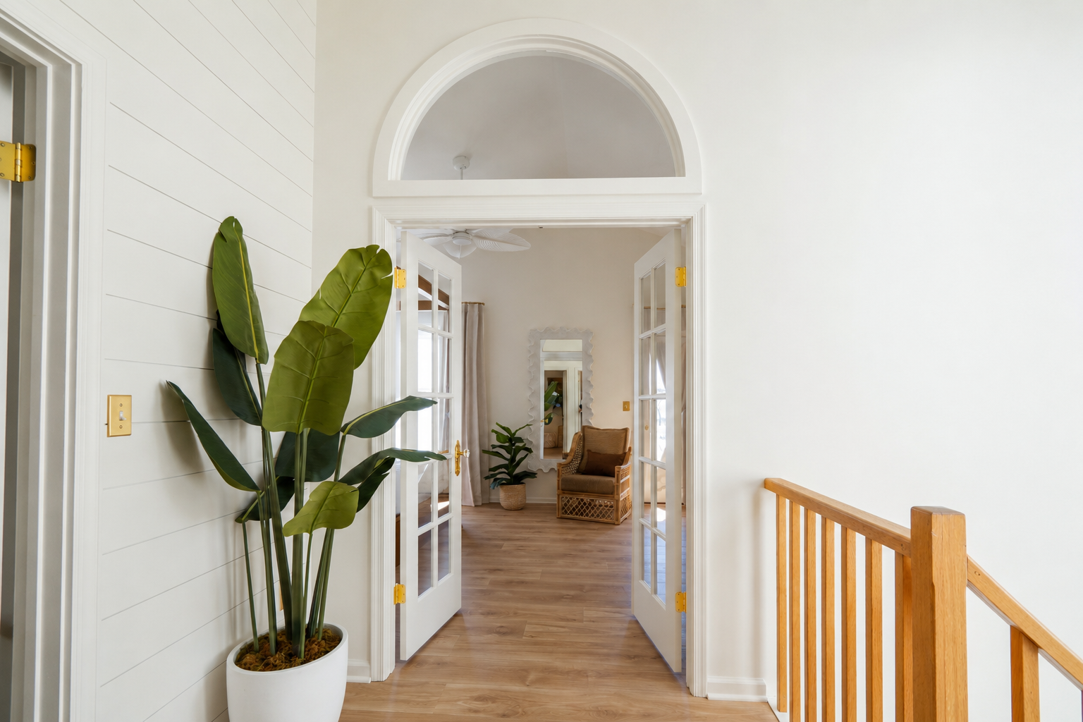 Bright hallway with white walls, arched doorway, wood floor, and potted plant near stairs
