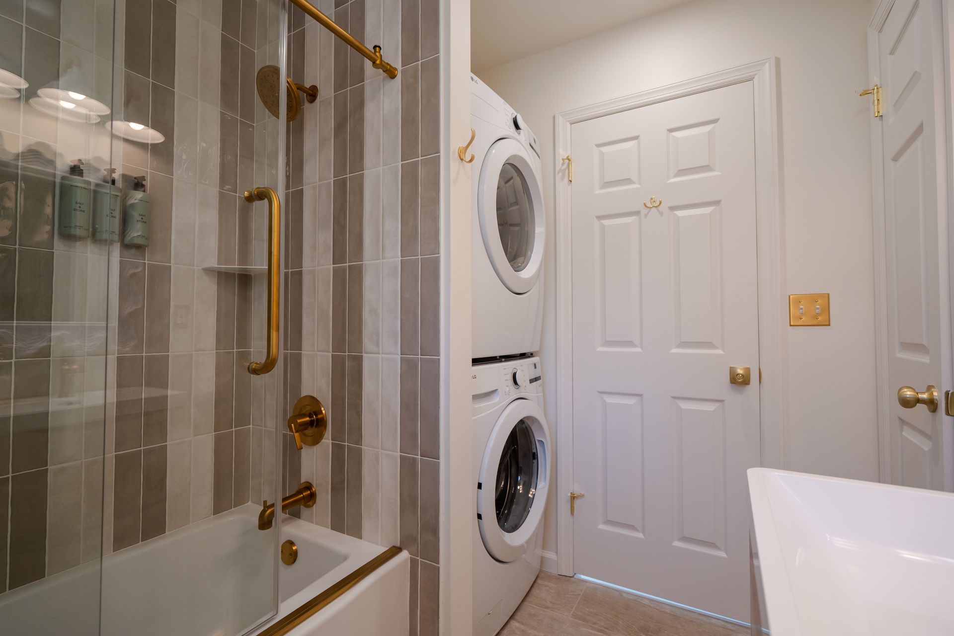 Small bathroom with glass shower, stacked washer and dryer, white door, and vanity sink