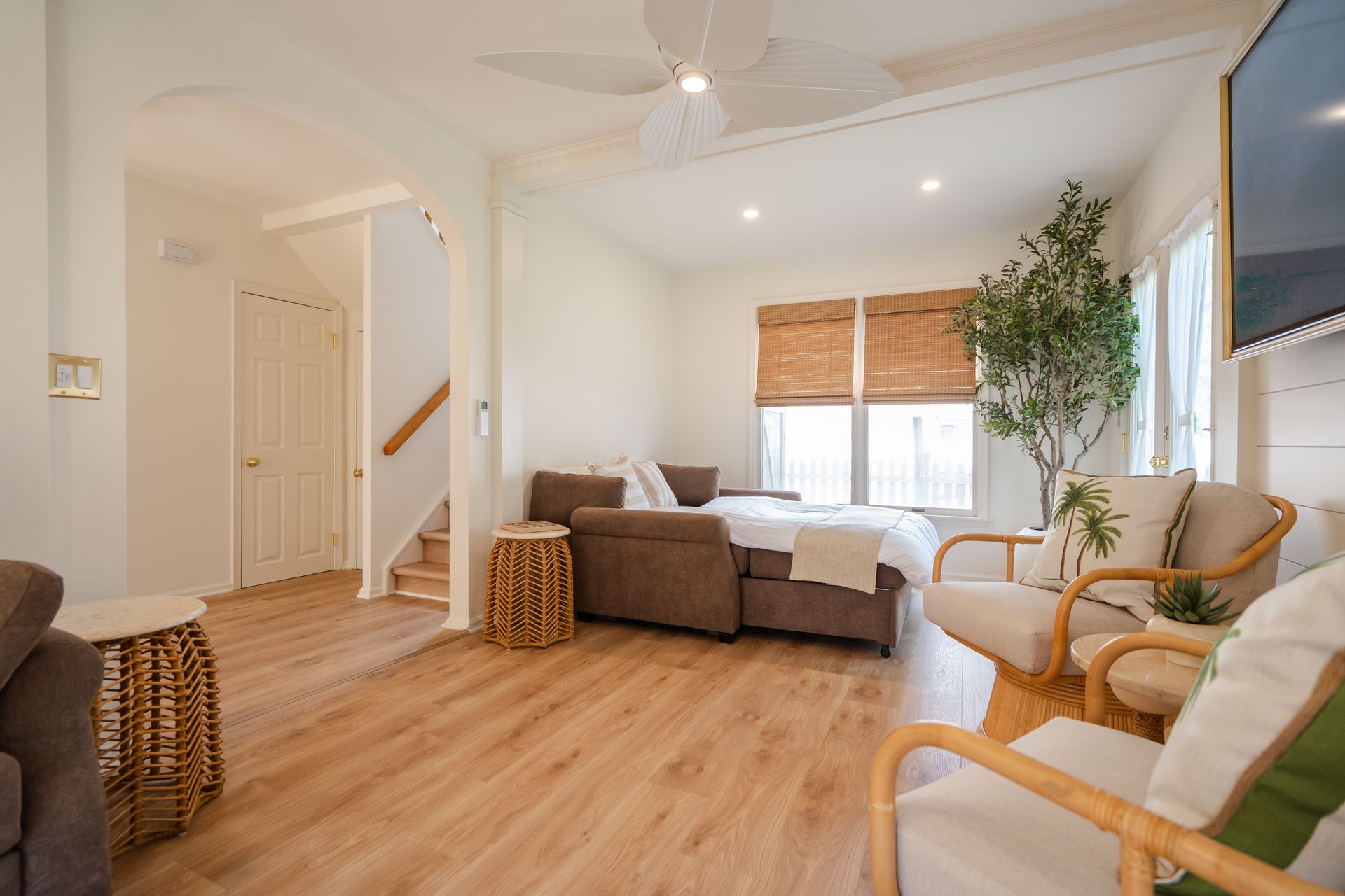 Bright living room with tan sofa, wicker chairs, wood floor, and large windows with blinds.