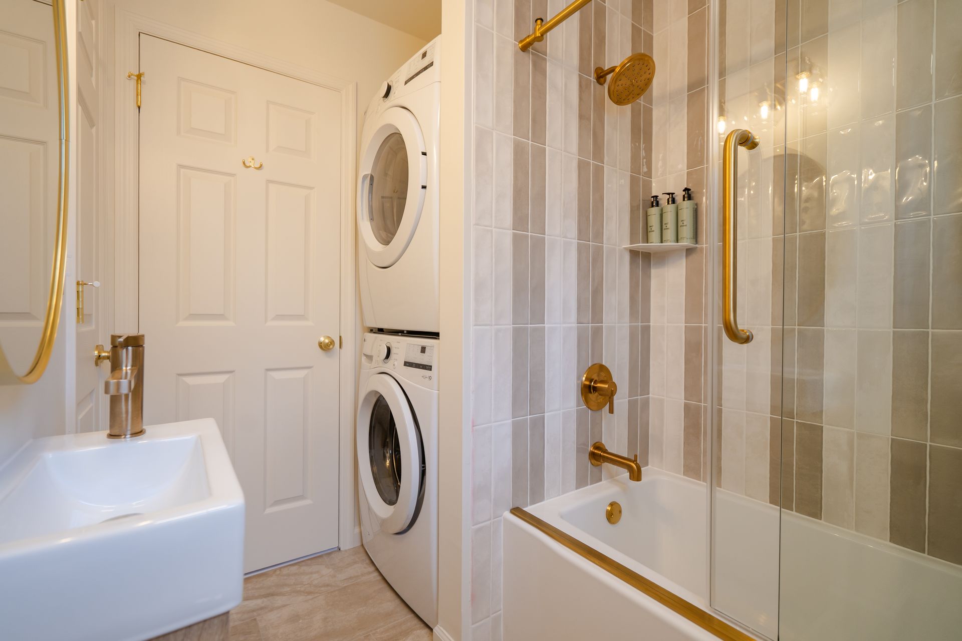 Small bathroom with stacked washer and dryer, white sink, and glass-enclosed shower with gold fixtures