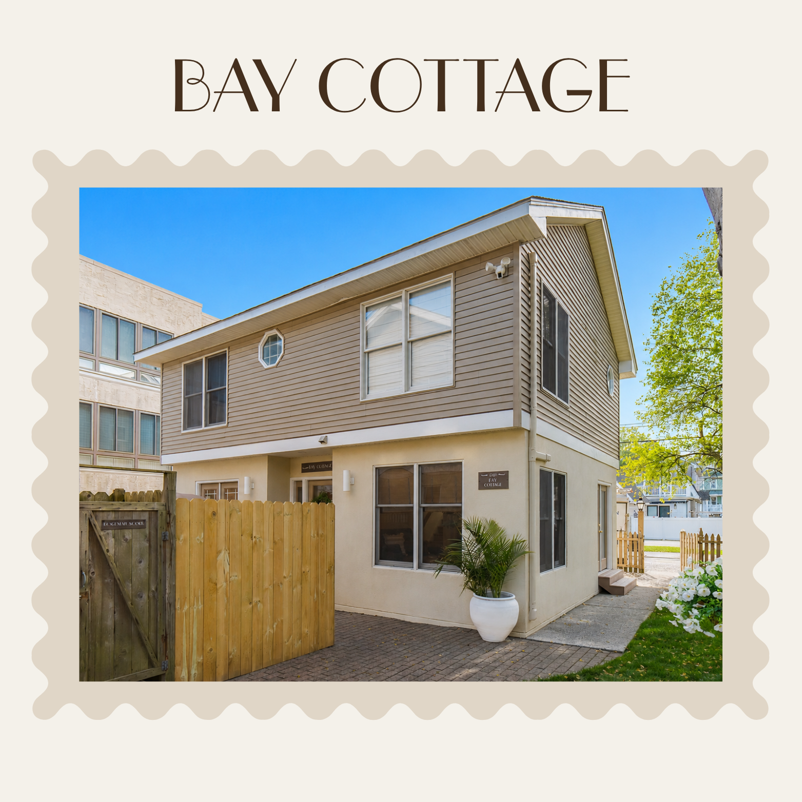 Two-story beige cottage with white trim, wood gate, and small garden under a blue sky