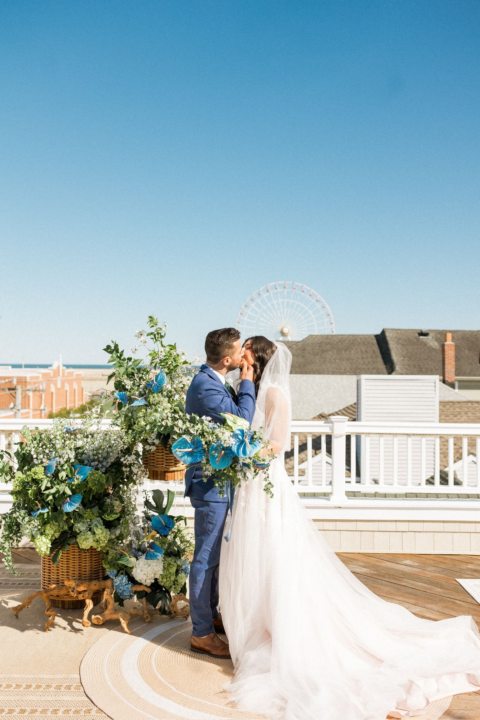 Couple kissing at an outdoor wedding ceremony; blue accents, sunny sky.
